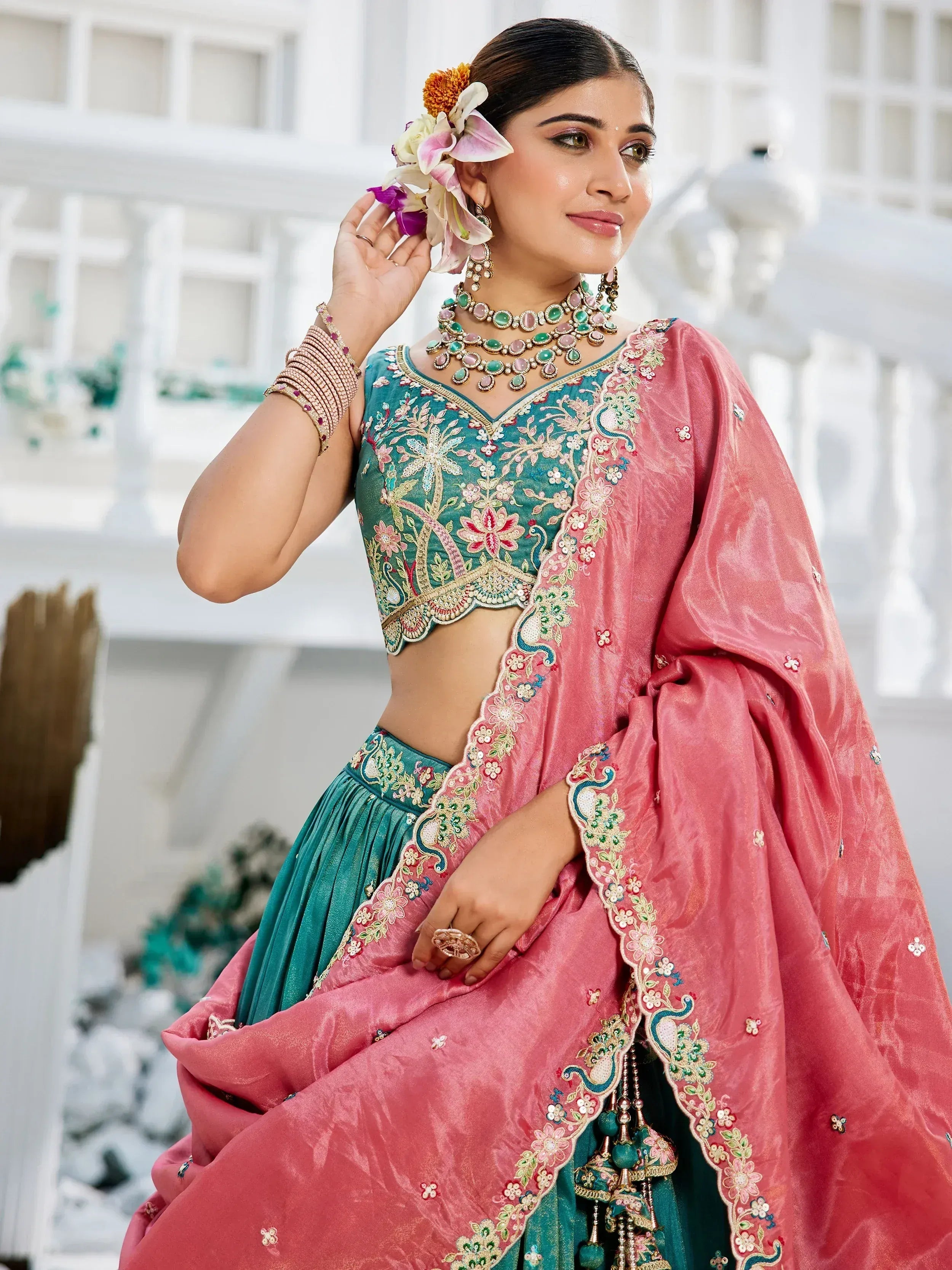 Teal and pink embroidered lehenga choli with floral jewelry, perfect for Indian ethnic wear events.