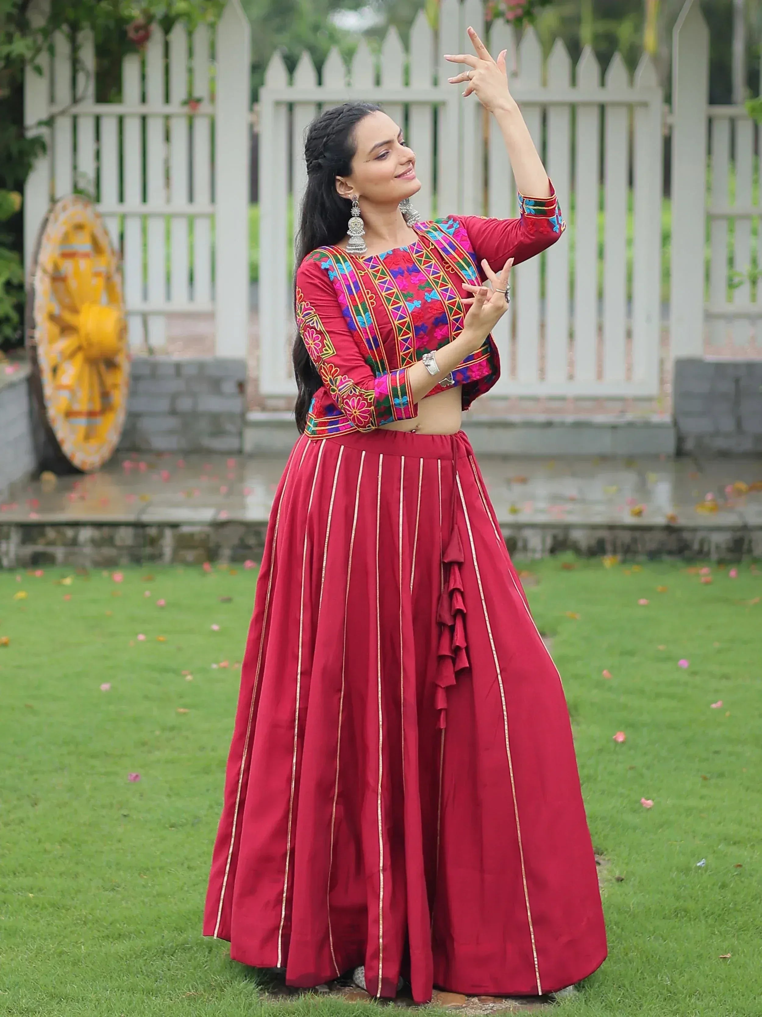 Woman in vibrant red embroidered lehenga choli, posing gracefully outdoors