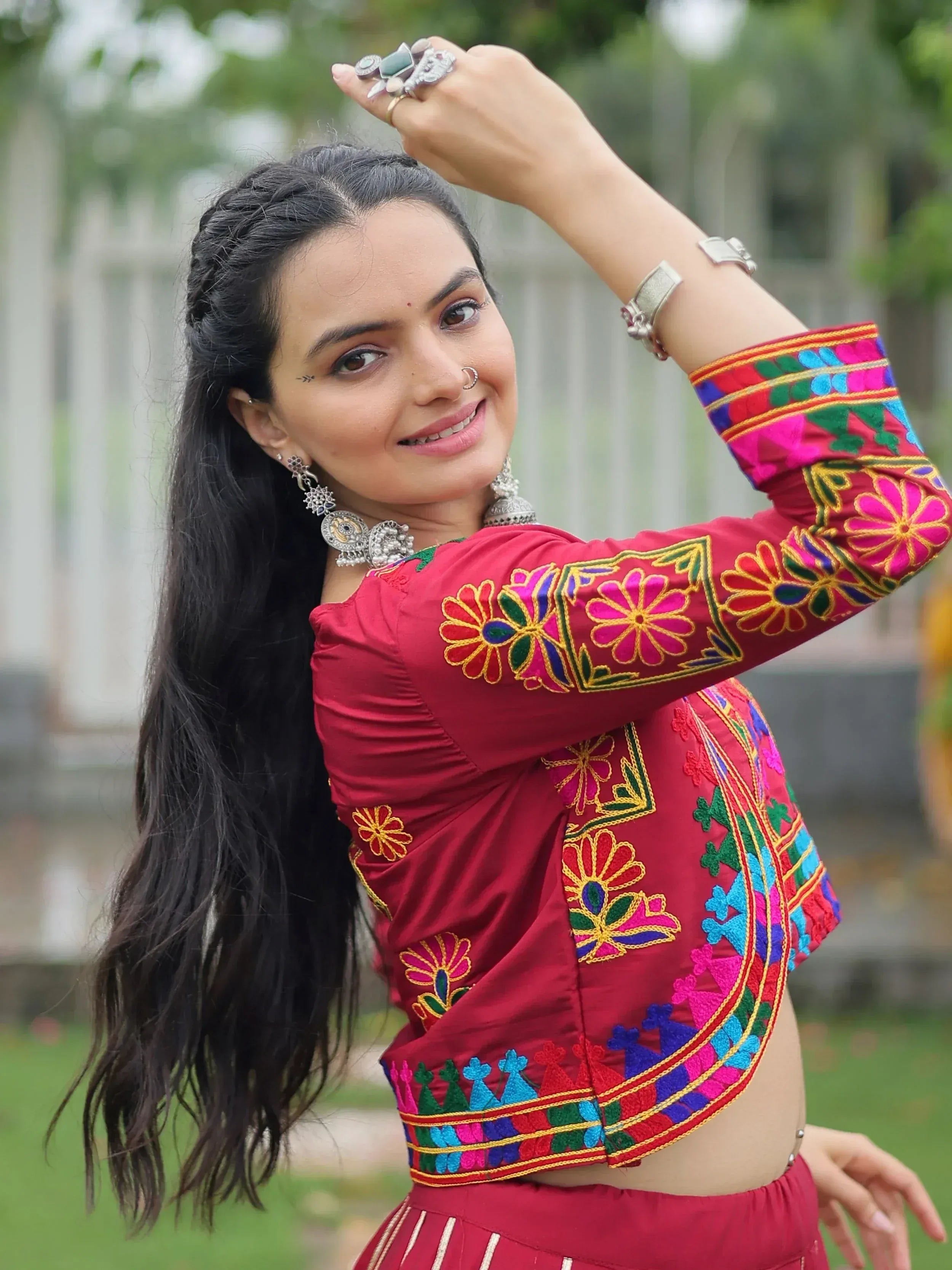 Woman in vibrant red embroidered ethnic top with floral patterns, traditional jewelry, and nose ring