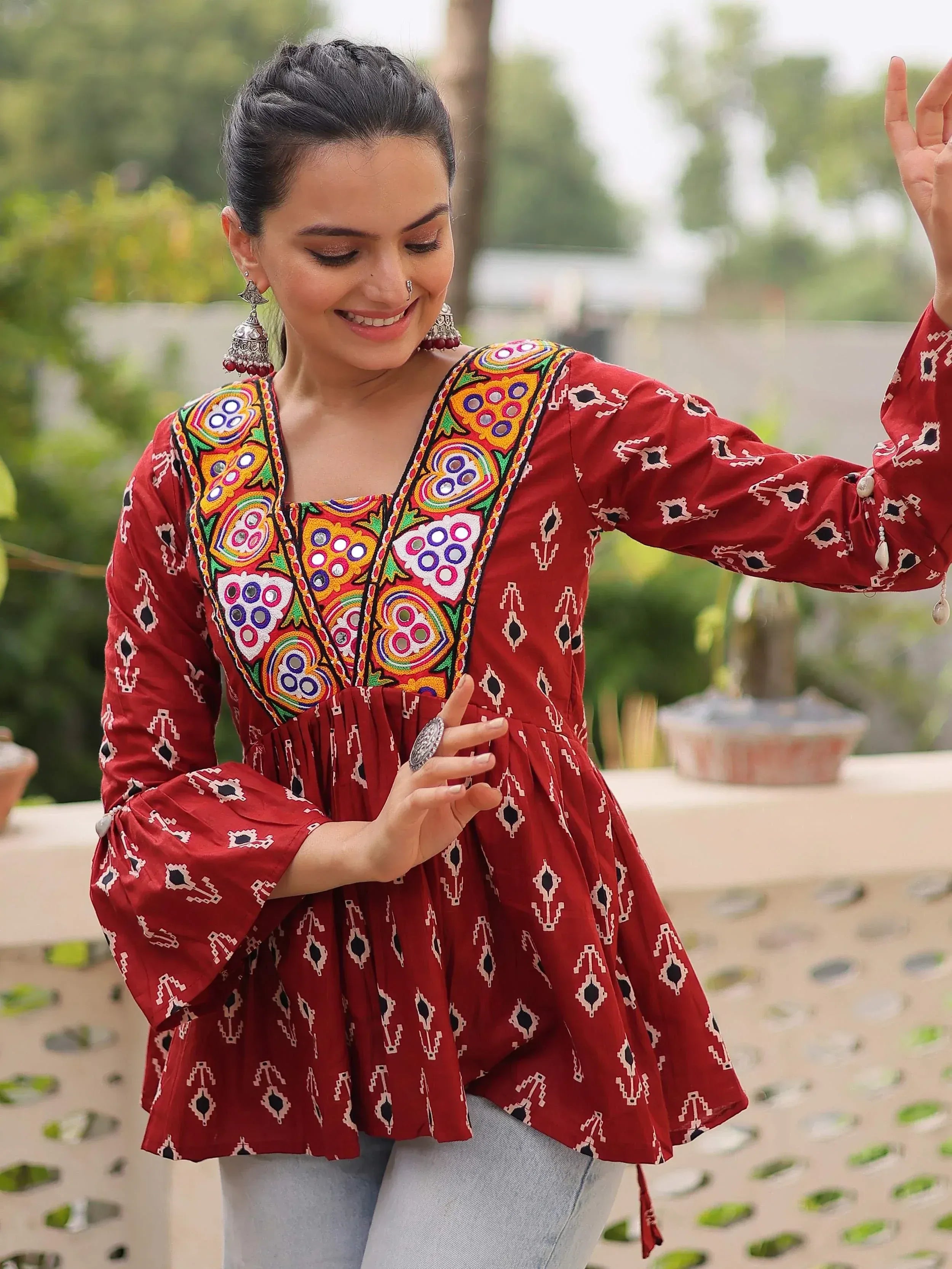 Red embroidered ethnic kurta with mirror work, bell sleeves, and geometric print, paired with jeans for casual wear.
