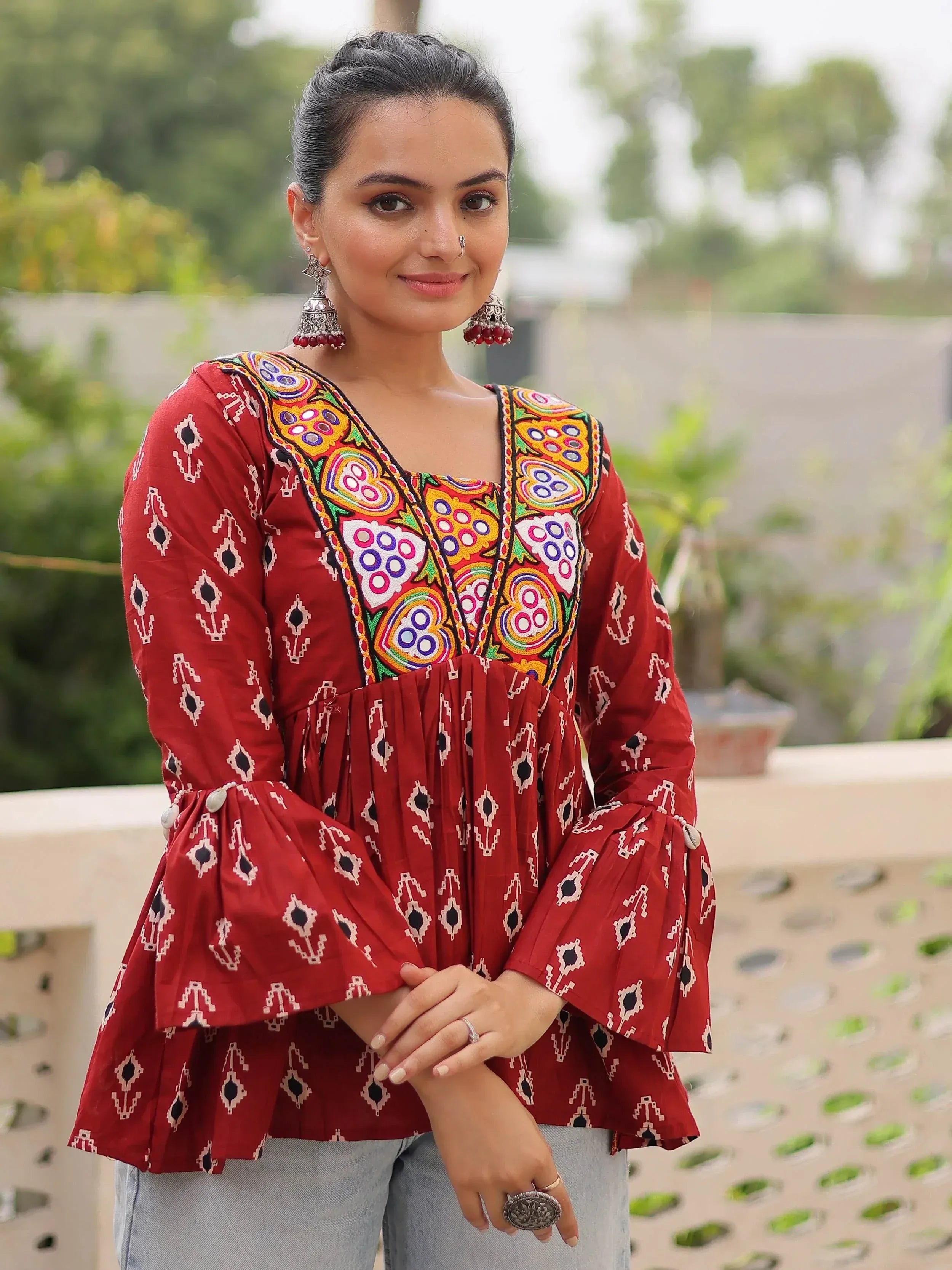 Red ethnic kurti with colorful embroidery and bell sleeves, paired with jeans for casual wear