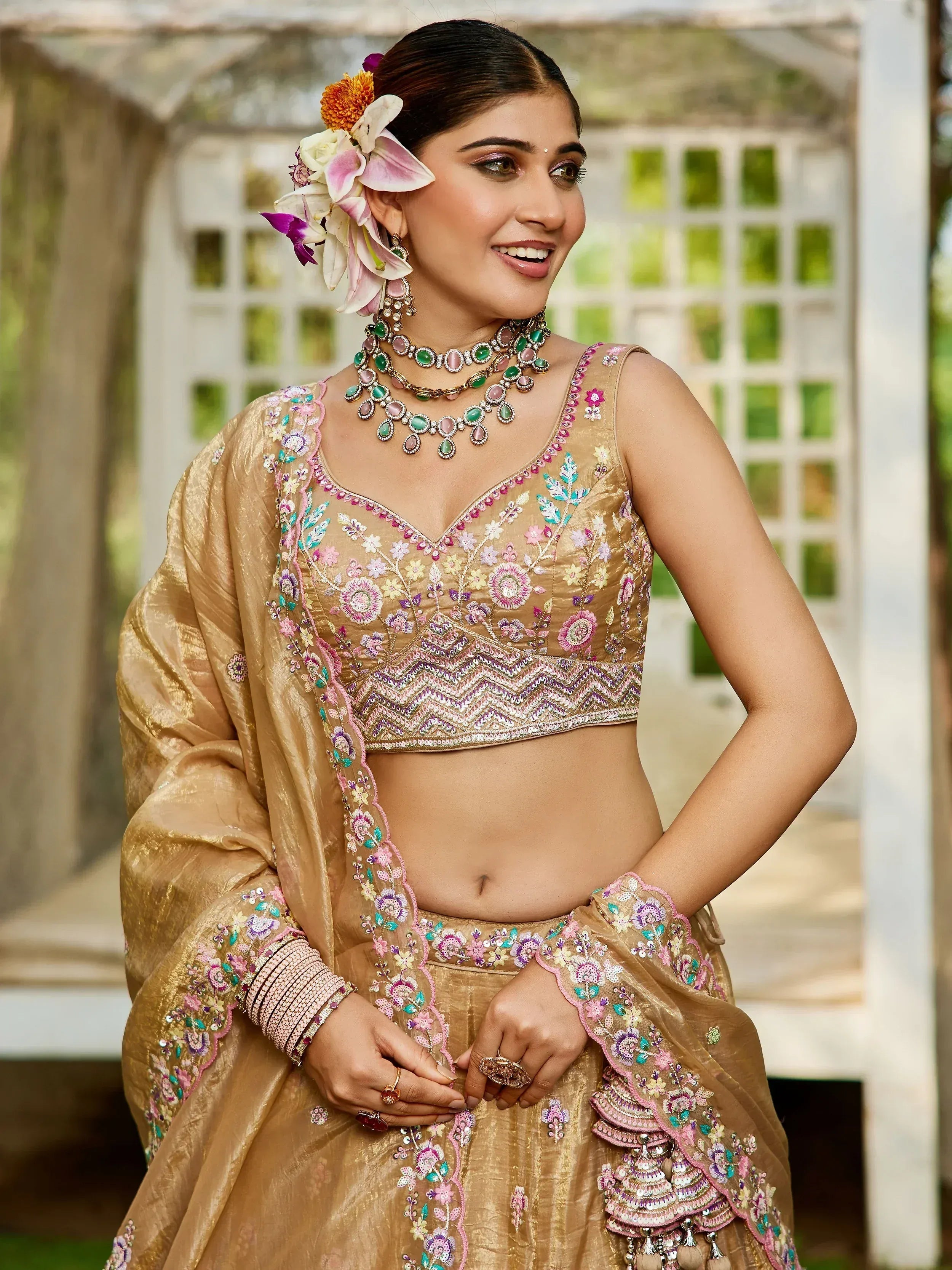 Woman in gold embroidered lehenga choli with floral jewelry, perfect for Indian ethnic wear occasions.