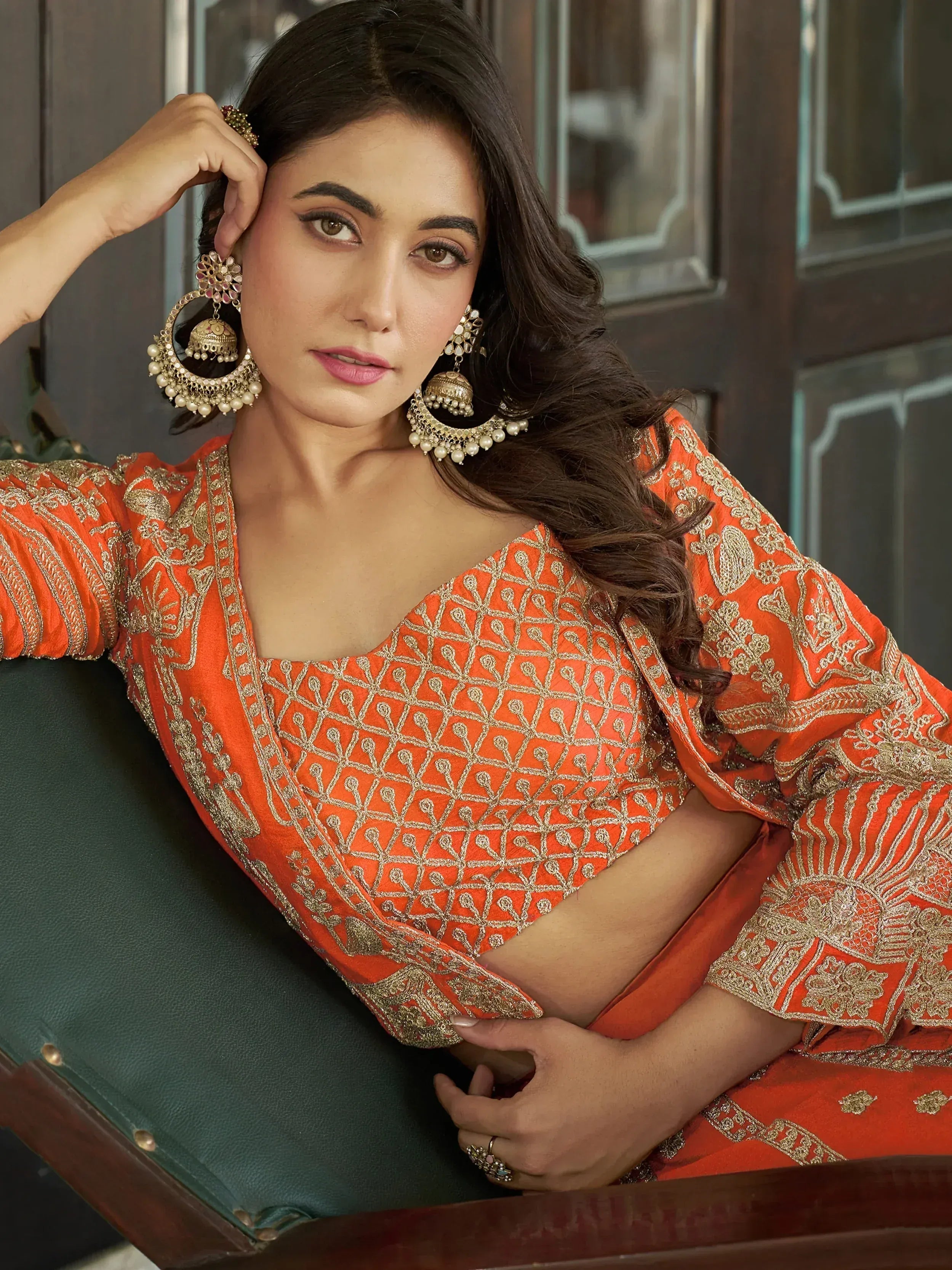 Woman in orange ethnic wear with gold embroidery and jhumka earrings, styled for festive occasions