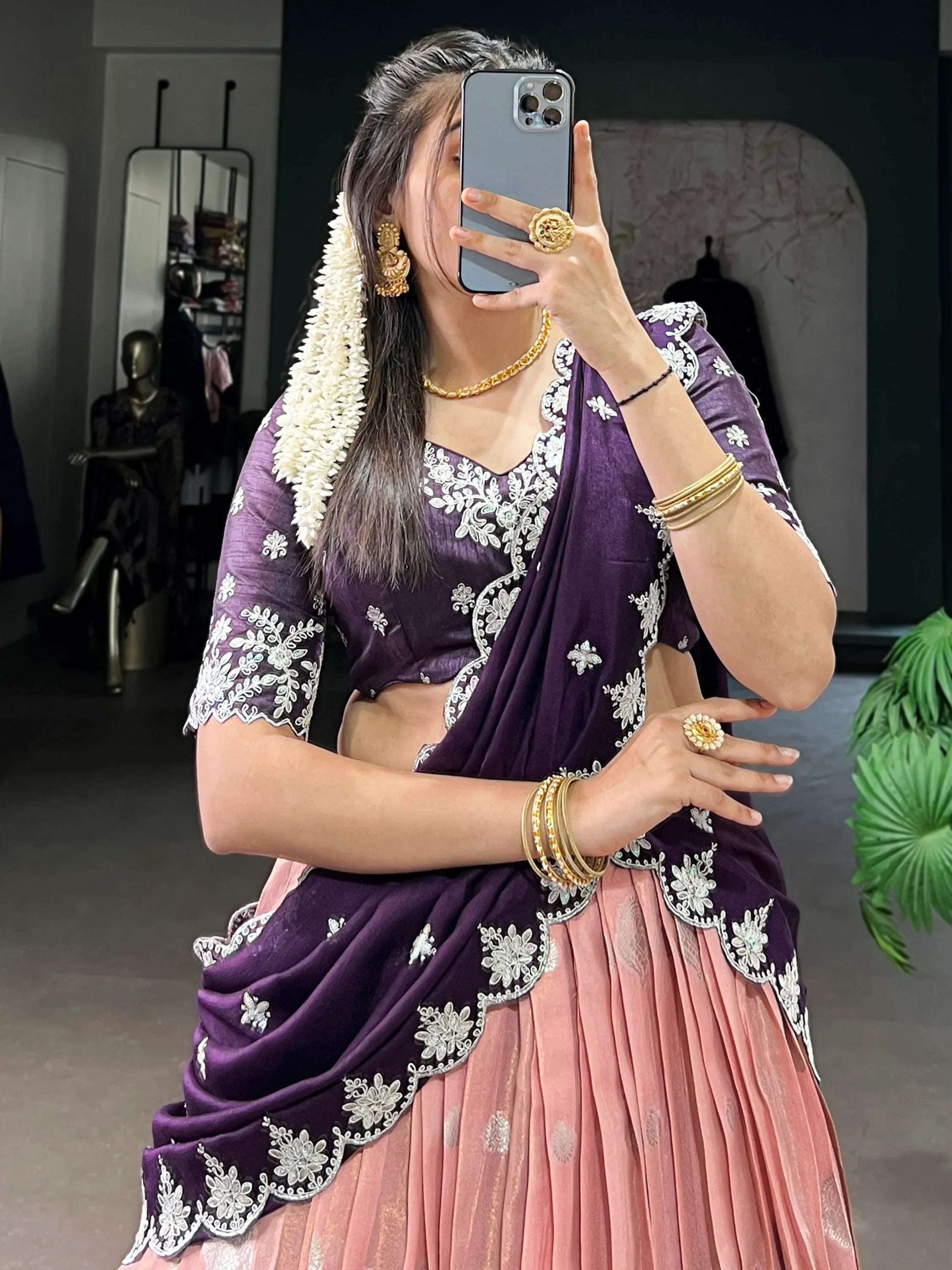 Woman in purple and pink embroidered lehenga choli with gold jewelry, taking mirror selfie