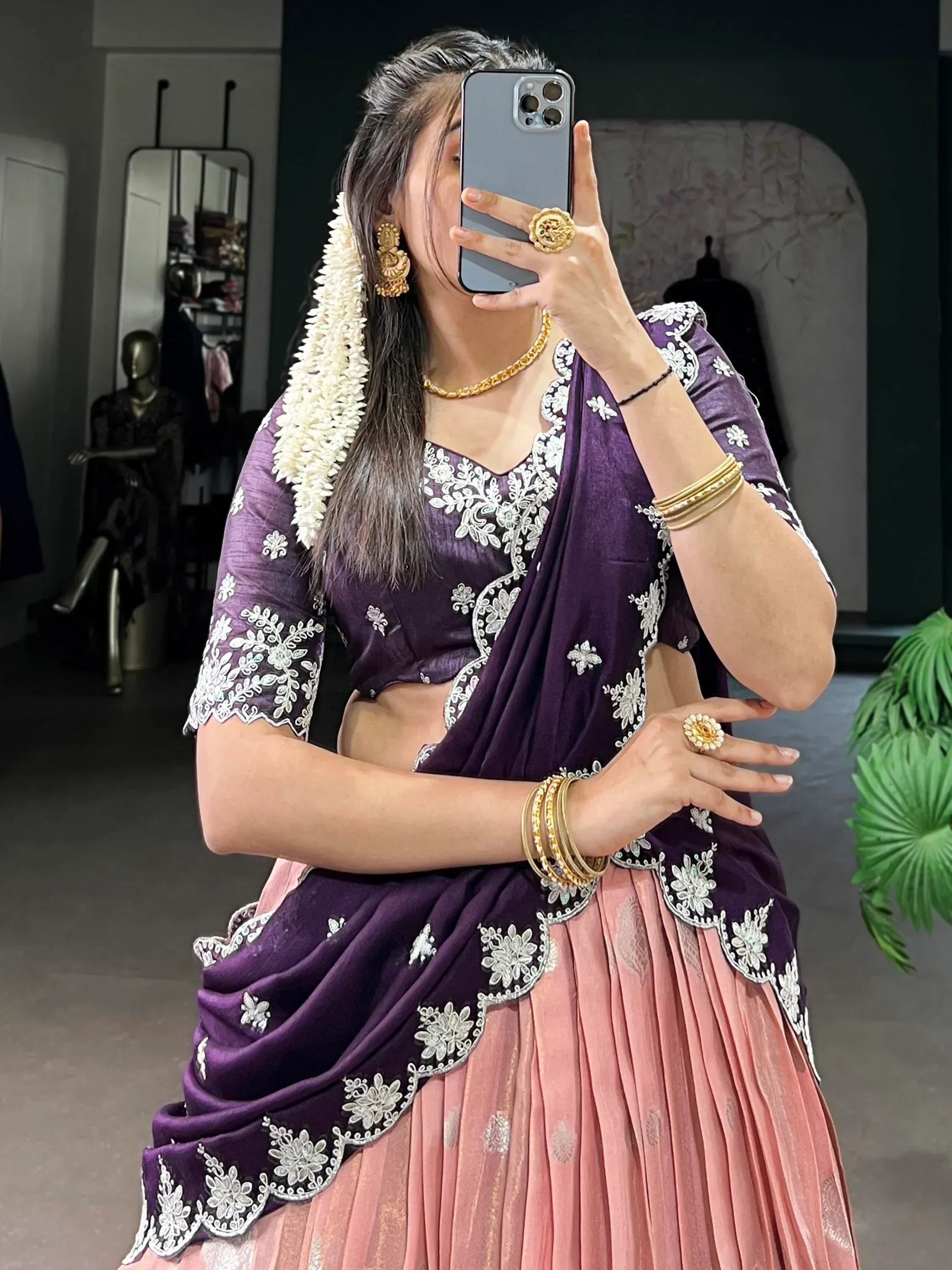 Woman in purple and pink embroidered lehenga choli with gold jewelry, taking mirror selfie