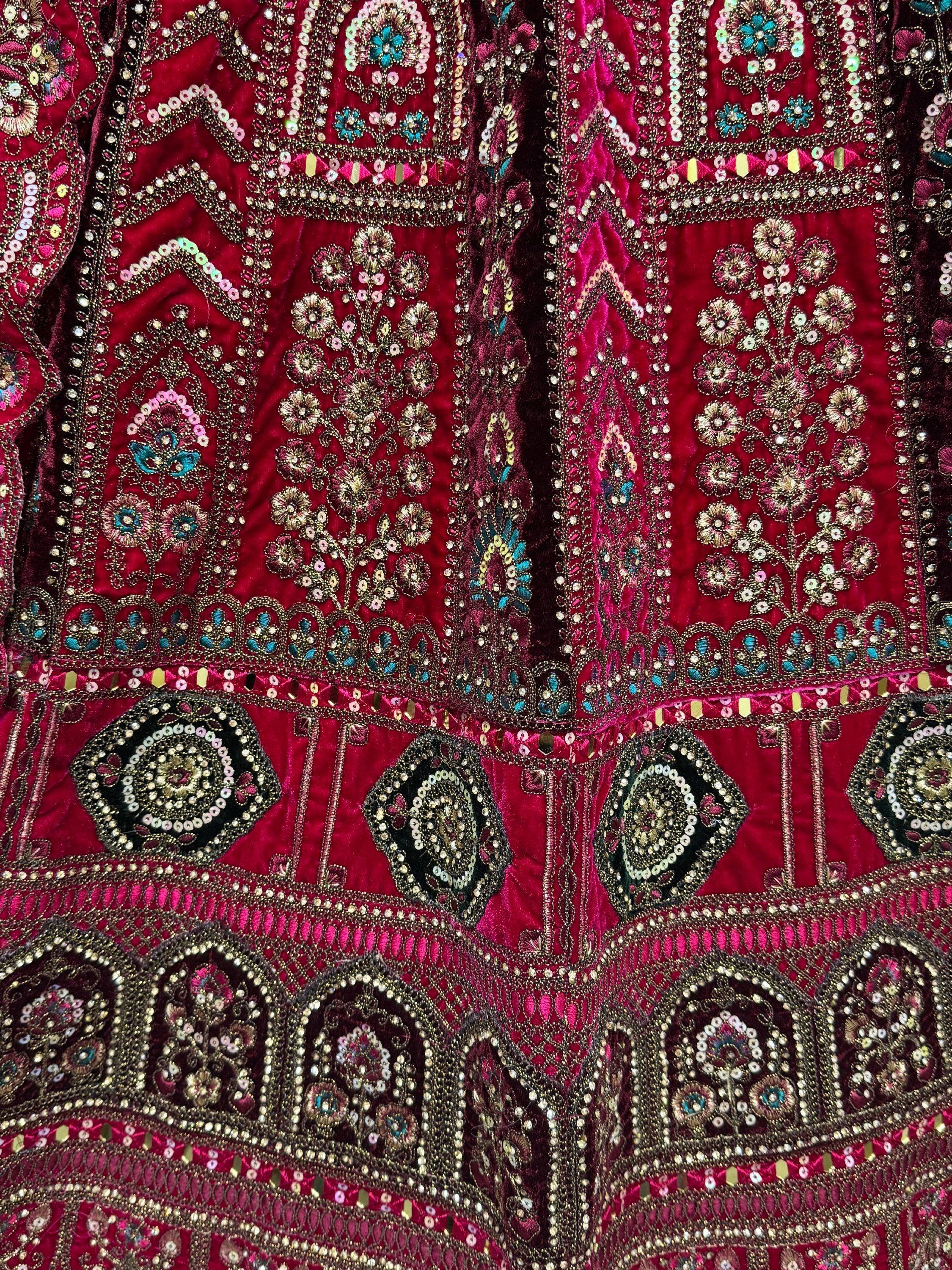 Richly embroidered maroon velvet lehenga with gold, pink, and blue floral motifs and mirror work.