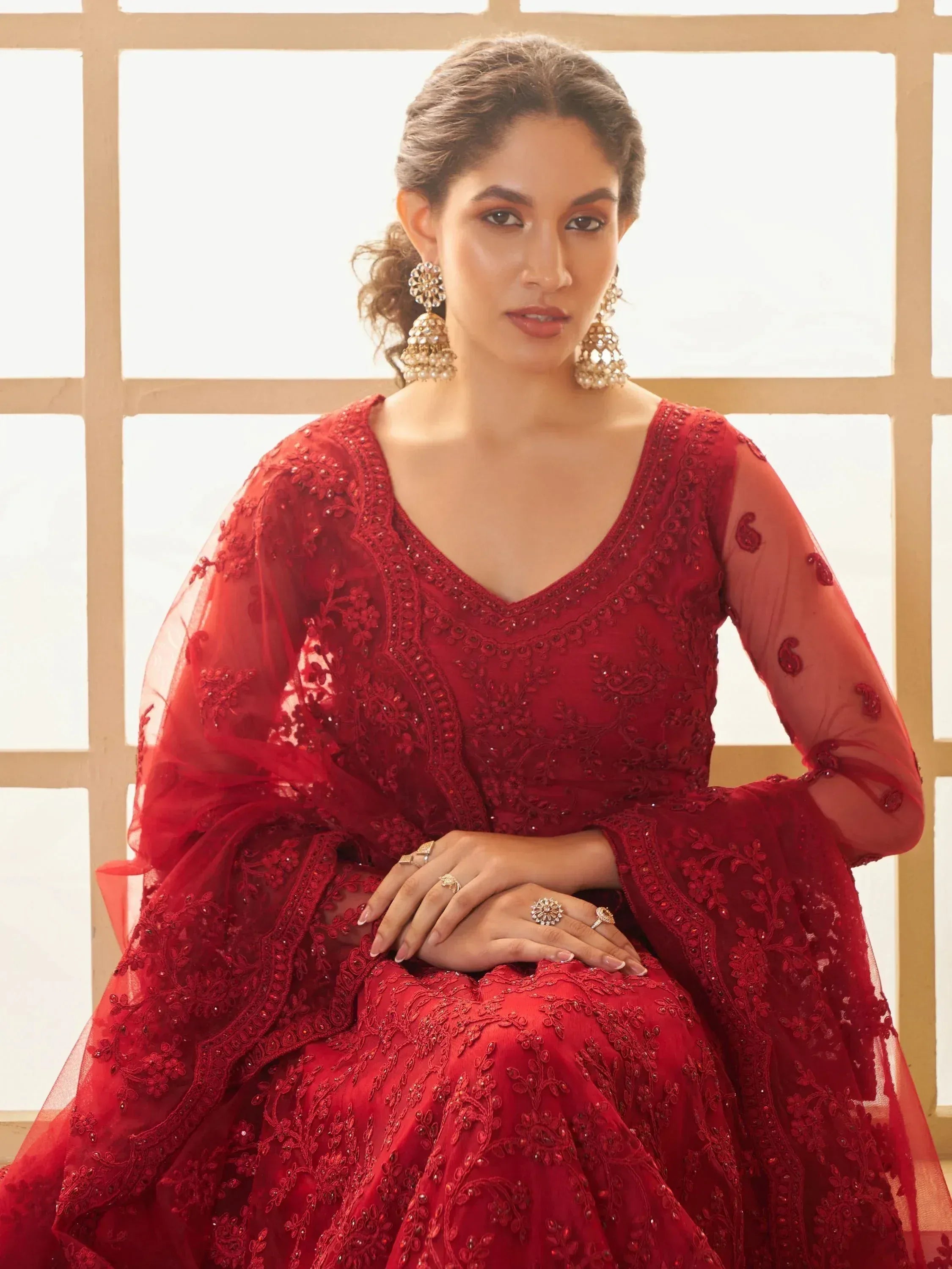 Elegant red embroidered ethnic gown with sheer sleeves and statement jewelry for festive occasions
