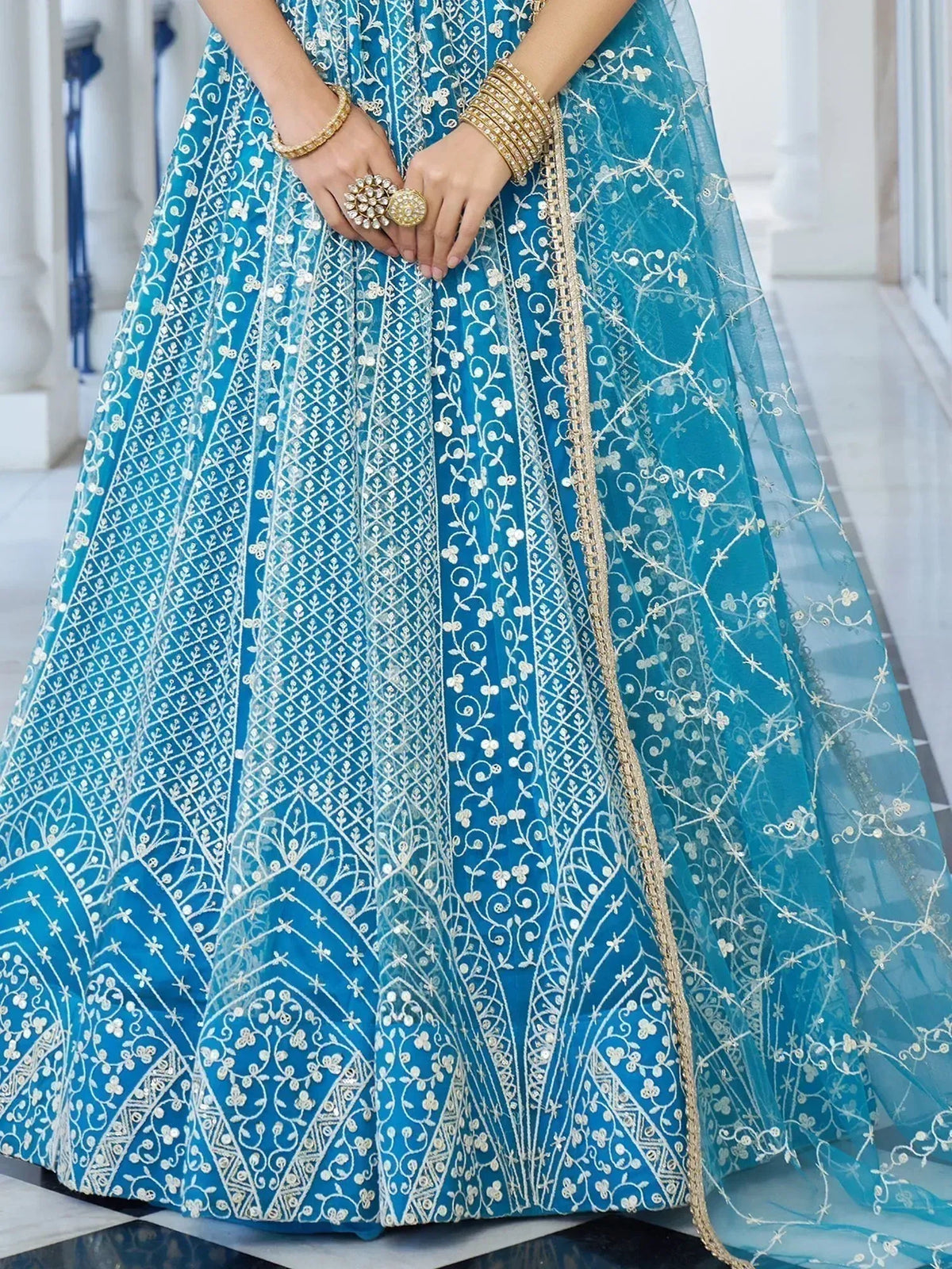 Turquoise designer lehenga with white floral embroidery and gold trim, paired with traditional Indian jewelry
