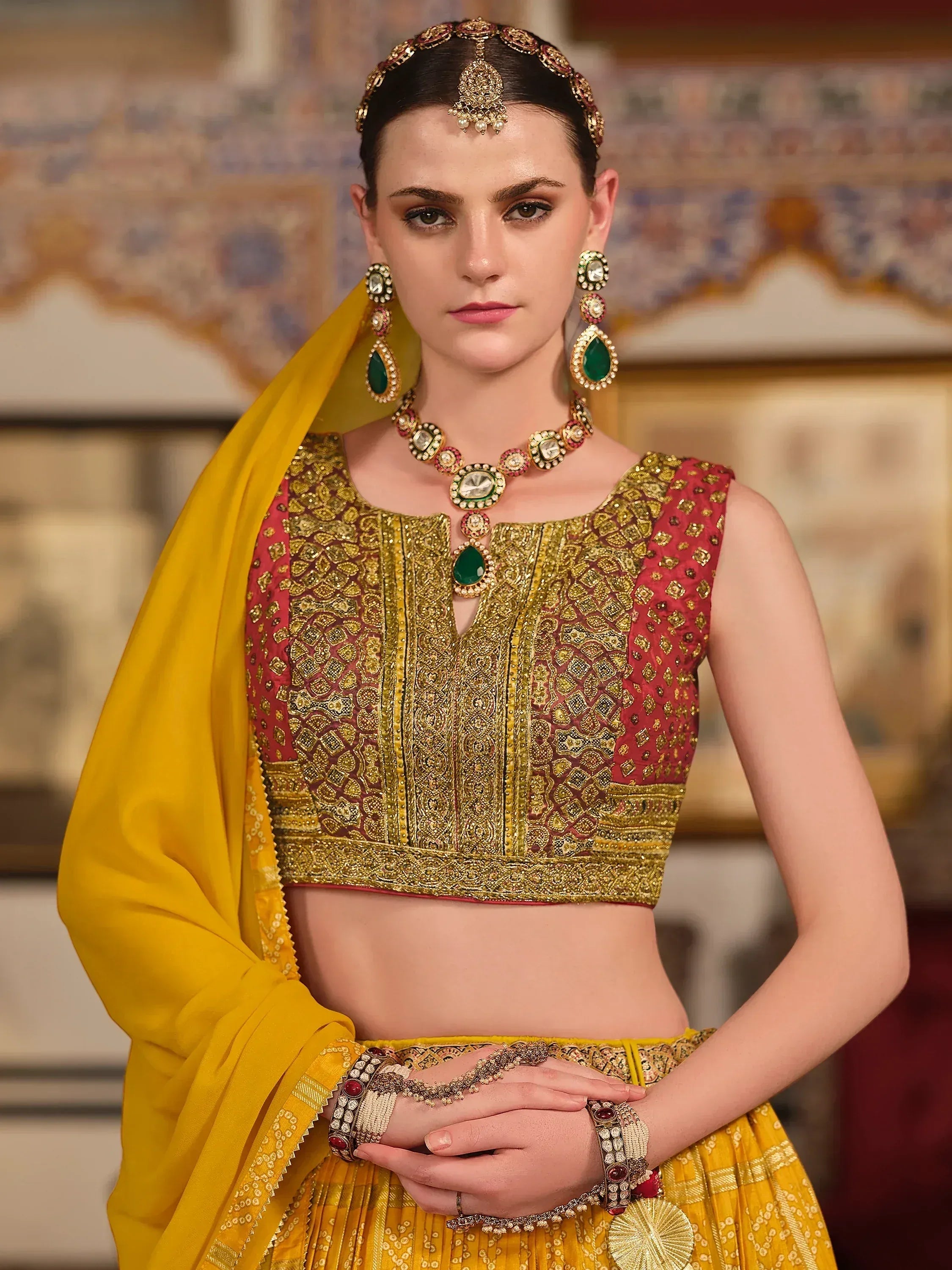 Elegant Indian lehenga choli with gold embroidery, red blouse, yellow dupatta, and traditional jewelry