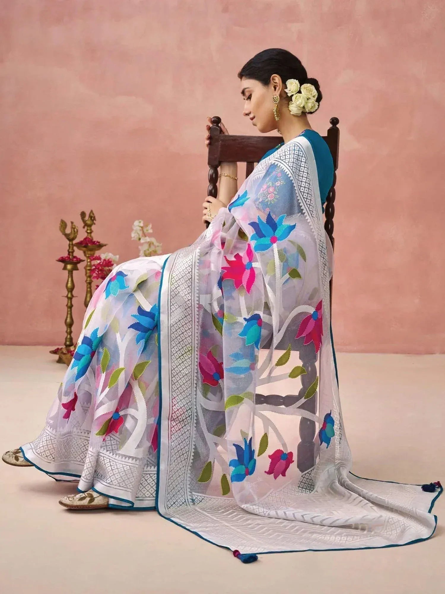 Woman in floral embroidered white saree with blue border, styled for ethnic occasions