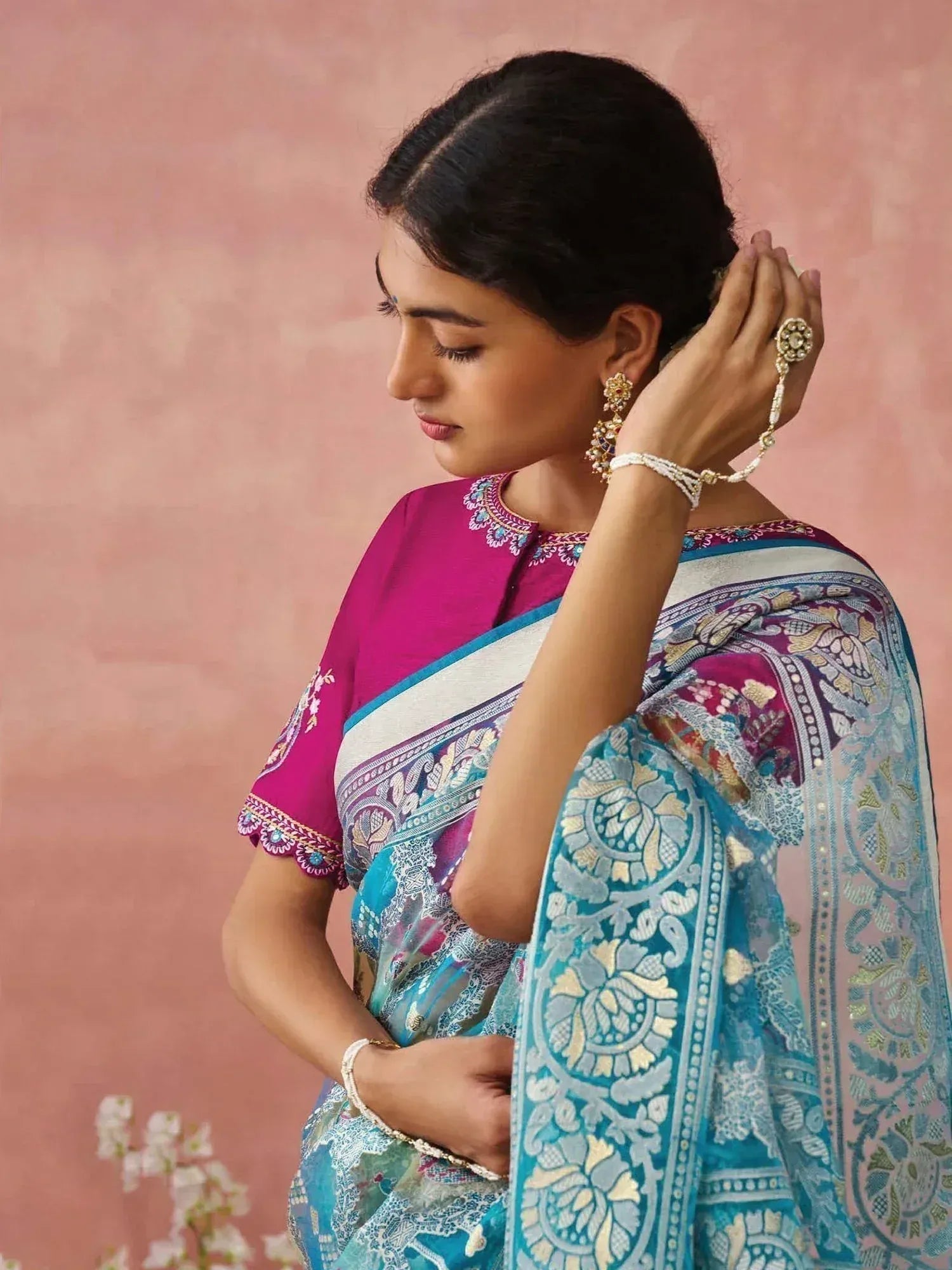 Woman in vibrant pink and blue embroidered saree with traditional jewelry, showcasing Indian ethnic wear