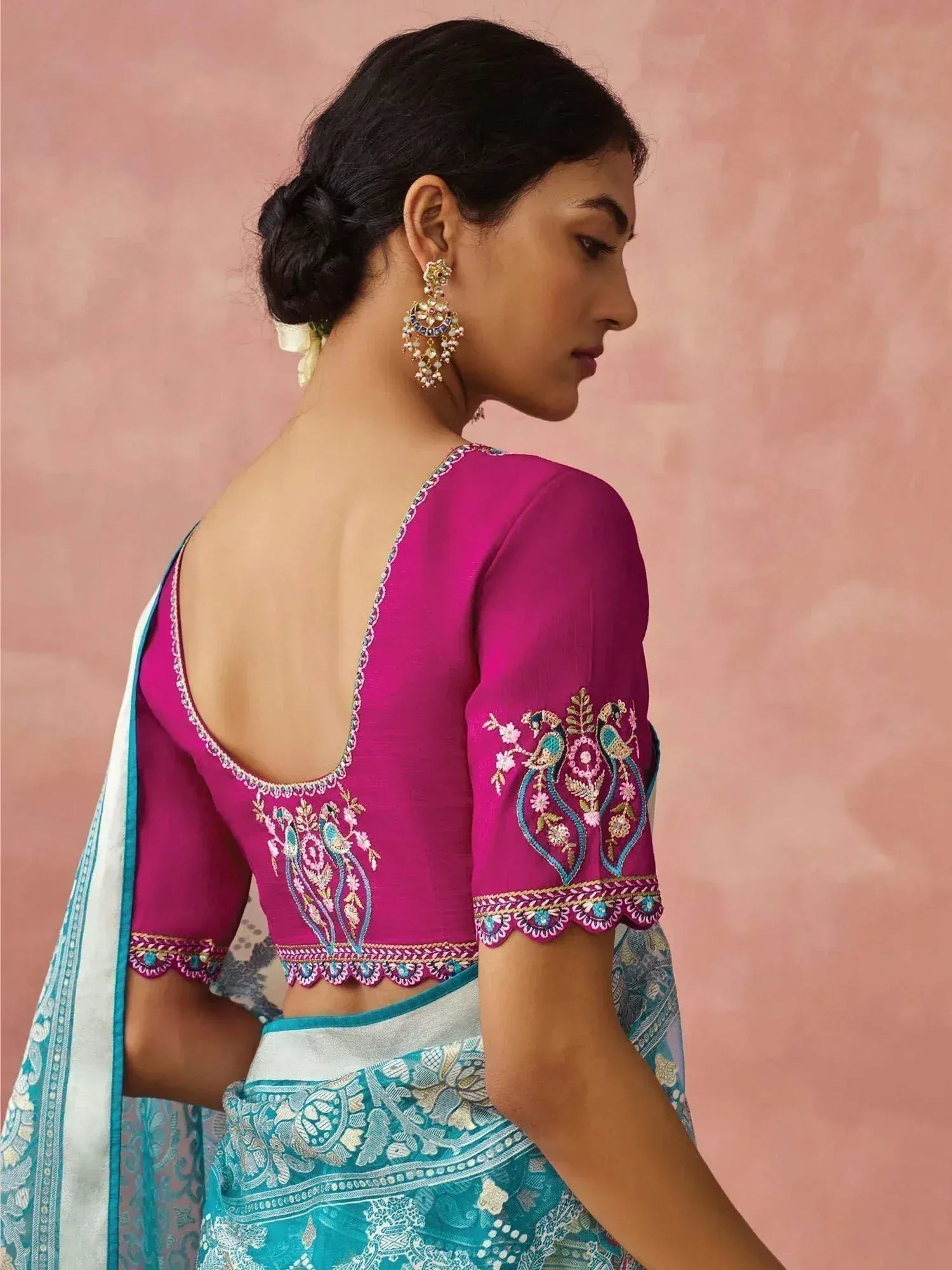 Pink embroidered blouse with peacock design, paired with teal saree, showcasing ethnic Indian wear