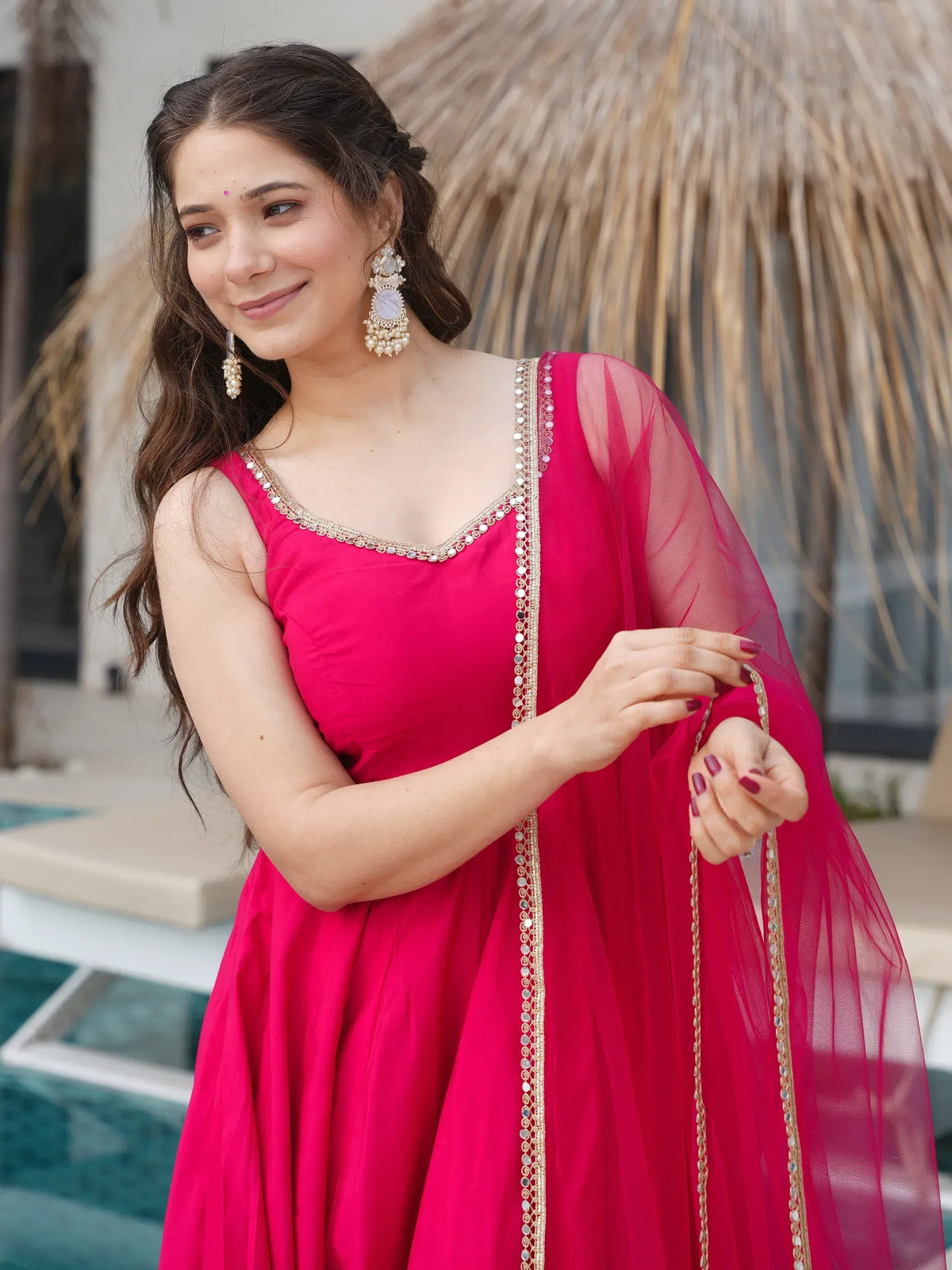 Woman in vibrant pink ethnic gown with gold mirror work, perfect for Indian celebrations and events.