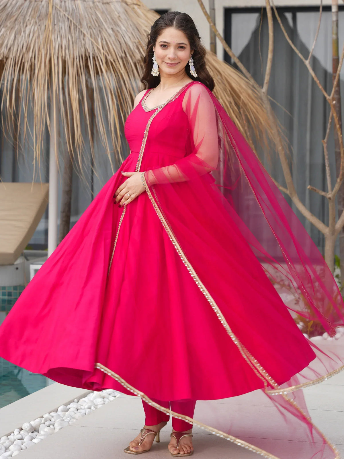 Woman in vibrant pink ethnic gown with sheer sleeves and gold trim, perfect for Indian occasions