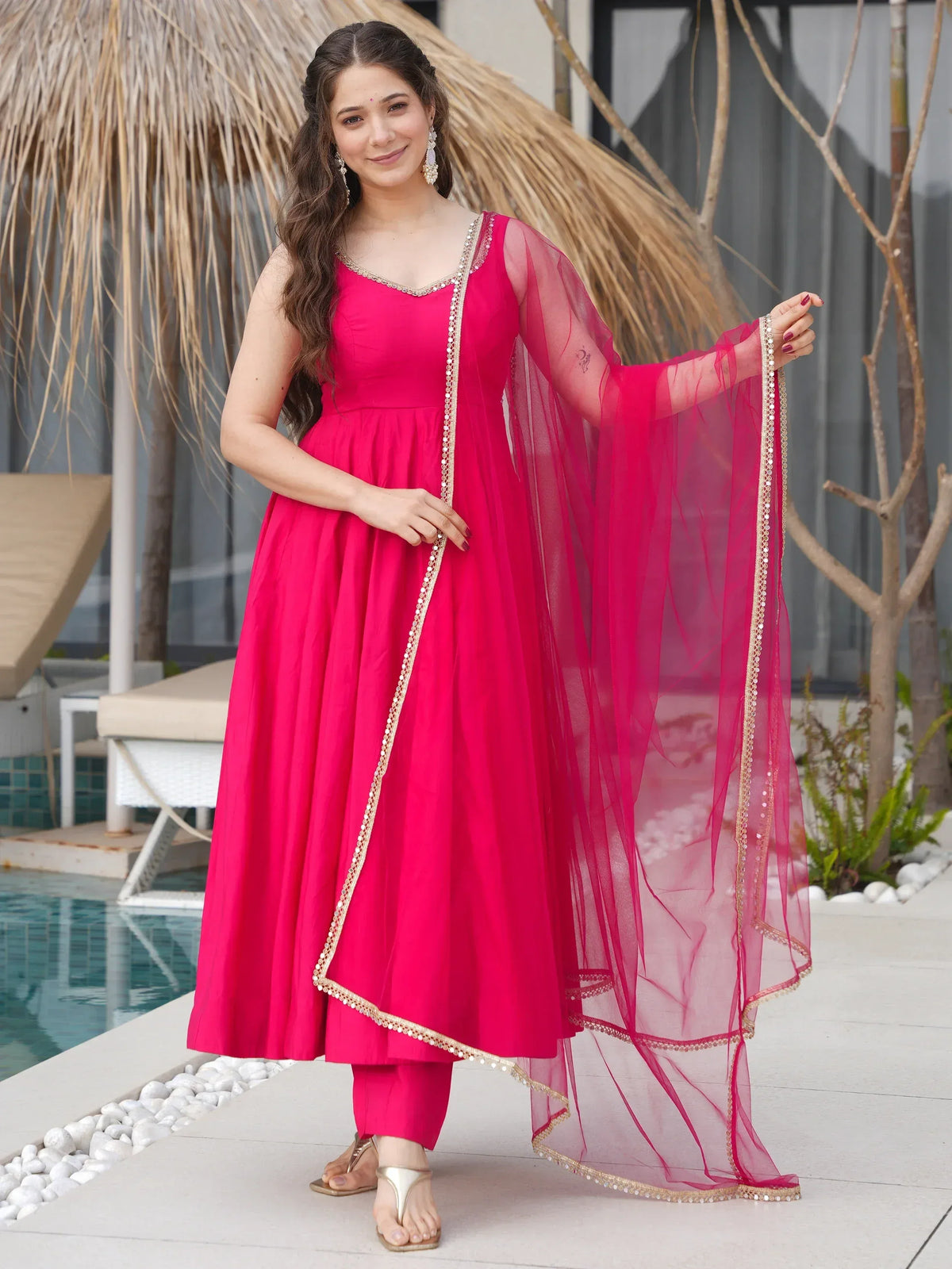 Vibrant pink ethnic anarkali suit with gold trim and sheer dupatta, perfect for festive occasions.