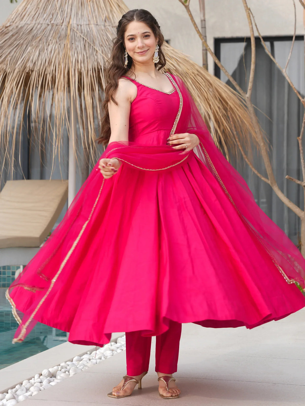Vibrant pink Indian ethnic gown with gold trim, paired with matching pants and dupatta, perfect for festive occasions.