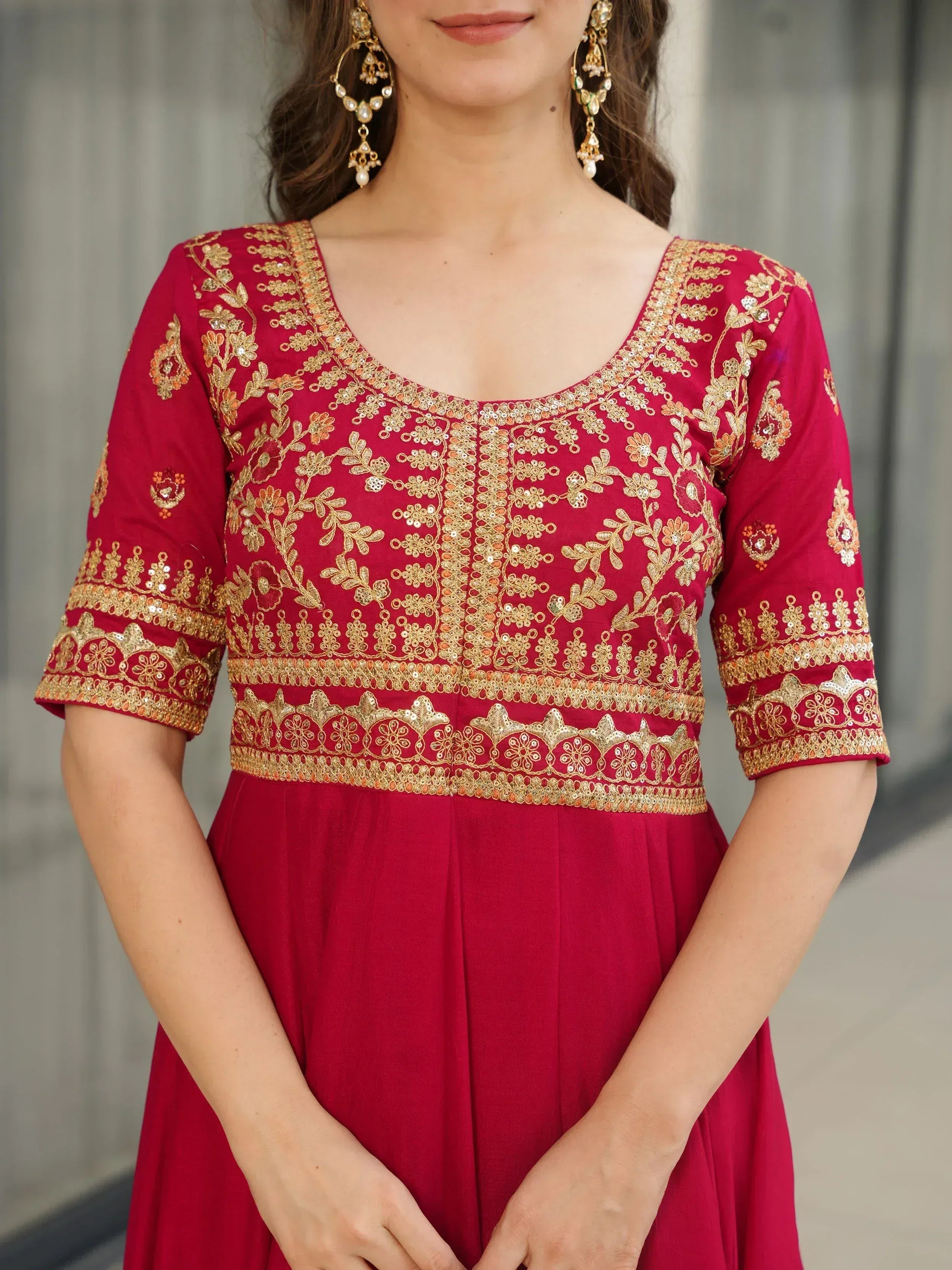 Red ethnic gown with gold floral embroidery and sequins, paired with traditional earrings