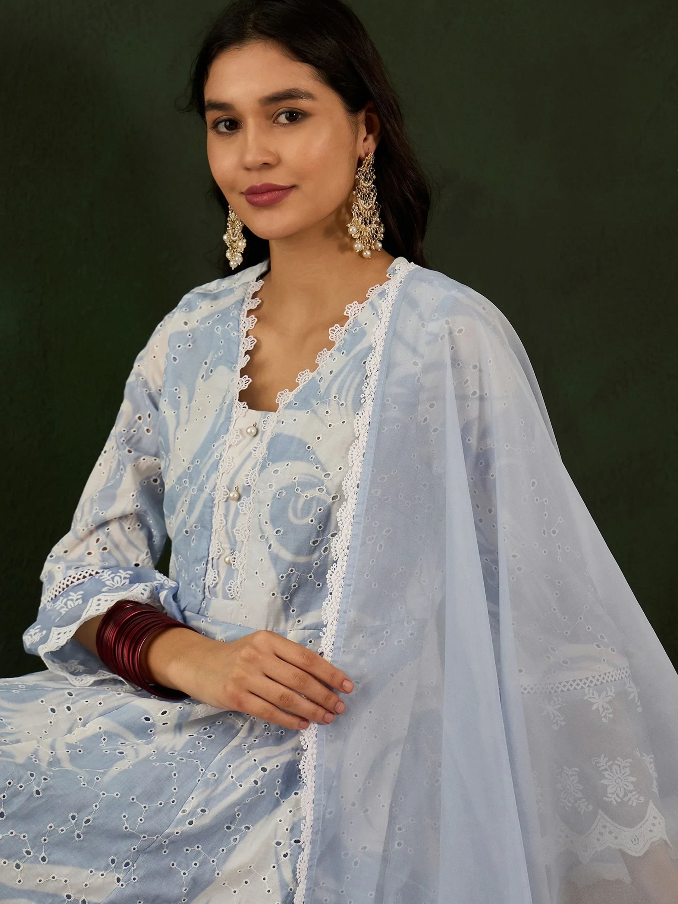 Woman wearing light blue embroidered salwar kameez with dupatta, statement earrings, red bangles