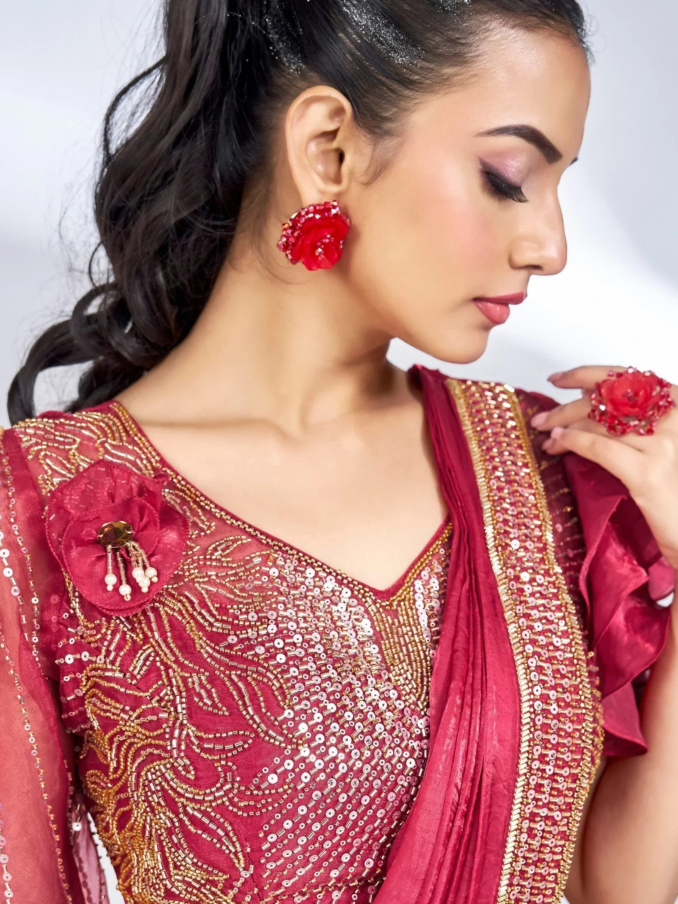 Woman in maroon ethnic gown with gold embroidery, floral earrings, and matching ring, perfect for Indian celebrations.