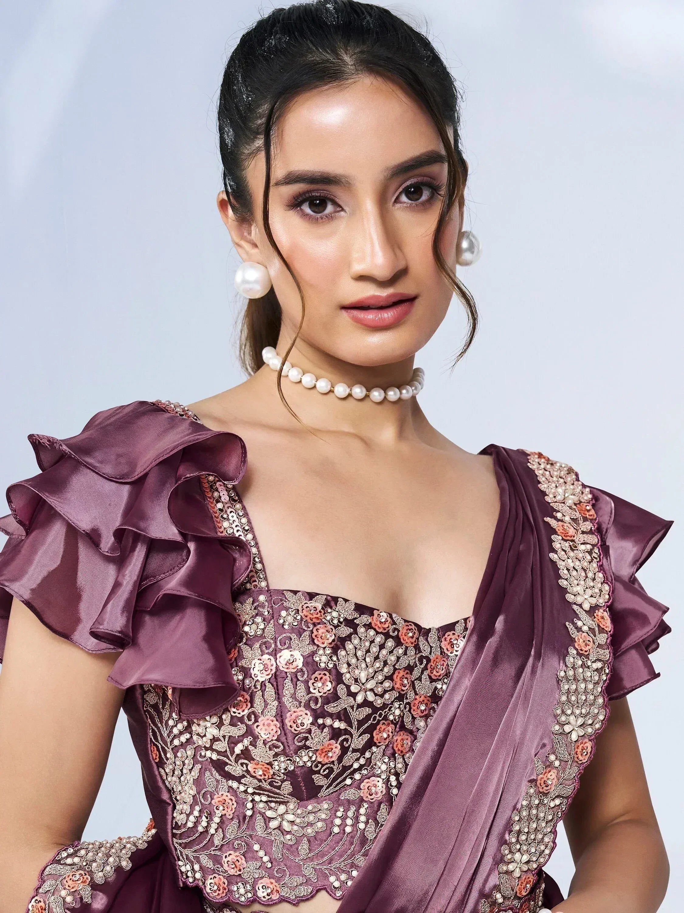 Elegant purple ethnic gown with floral embroidery, ruffle sleeves, and pearl jewelry for Indian occasions
