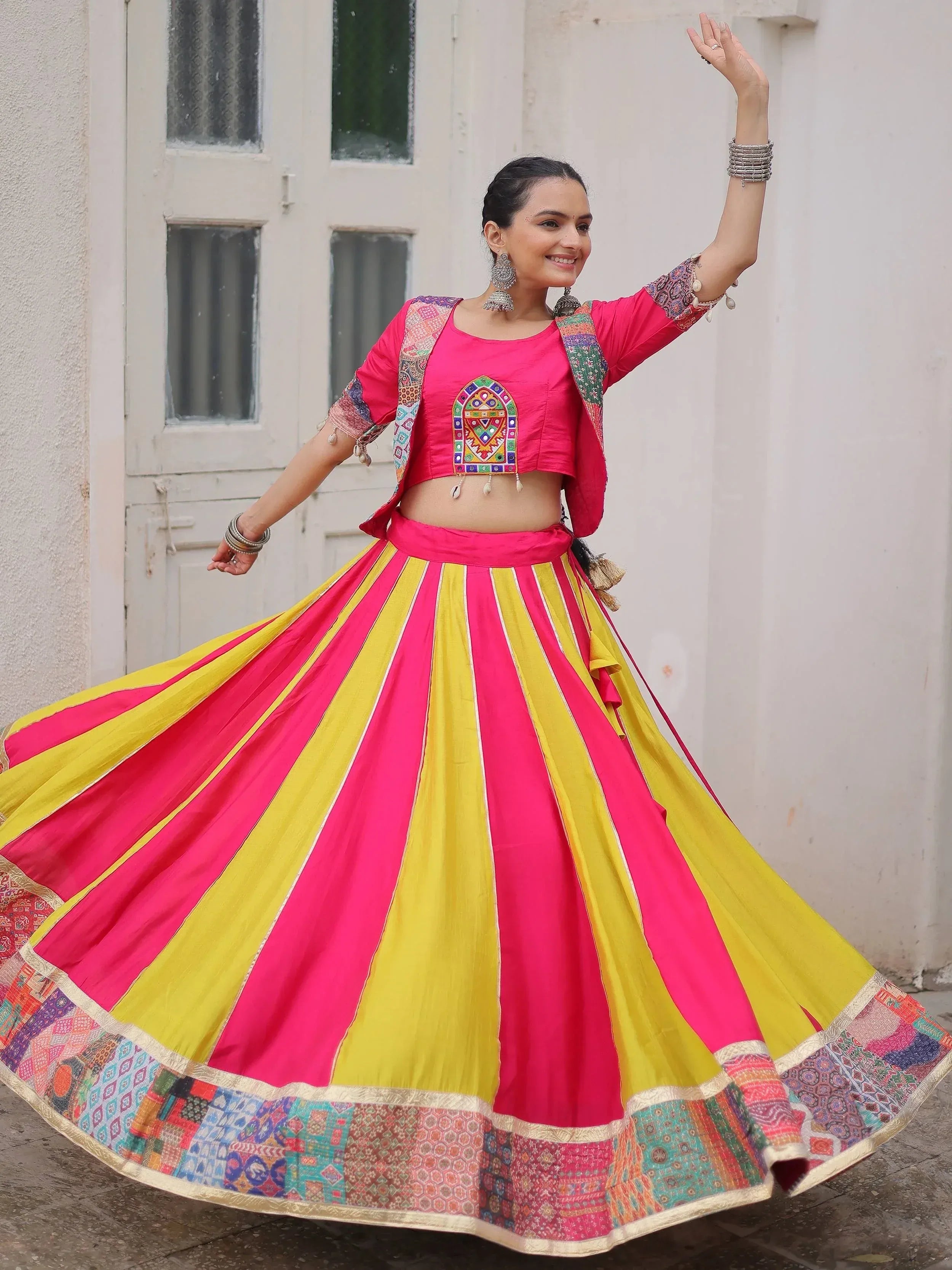 Woman in vibrant pink and yellow striped lehenga choli with mirror work, dancing outdoors