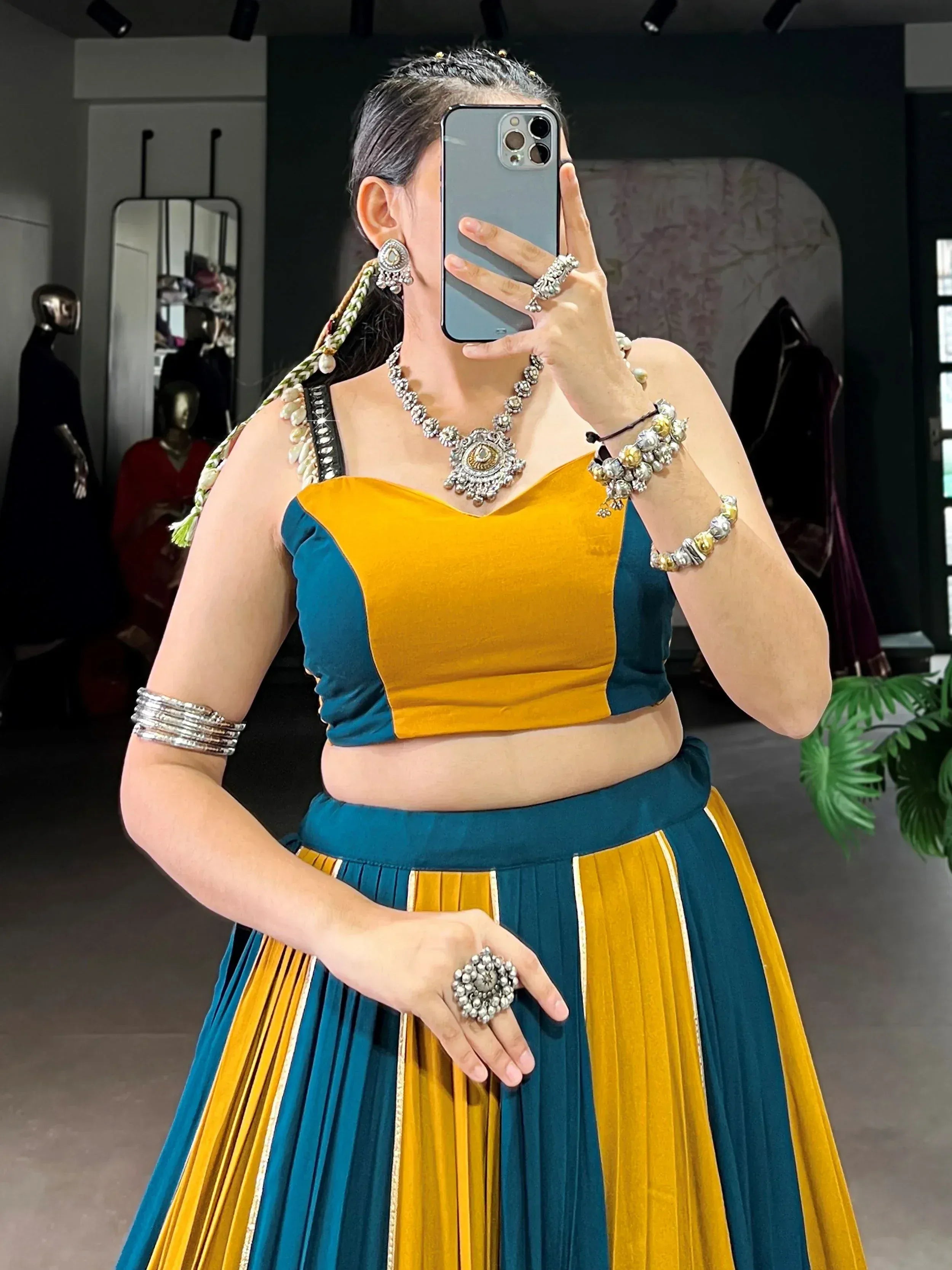 Woman in yellow and teal velvet lehenga choli with traditional jewelry, taking mirror selfie