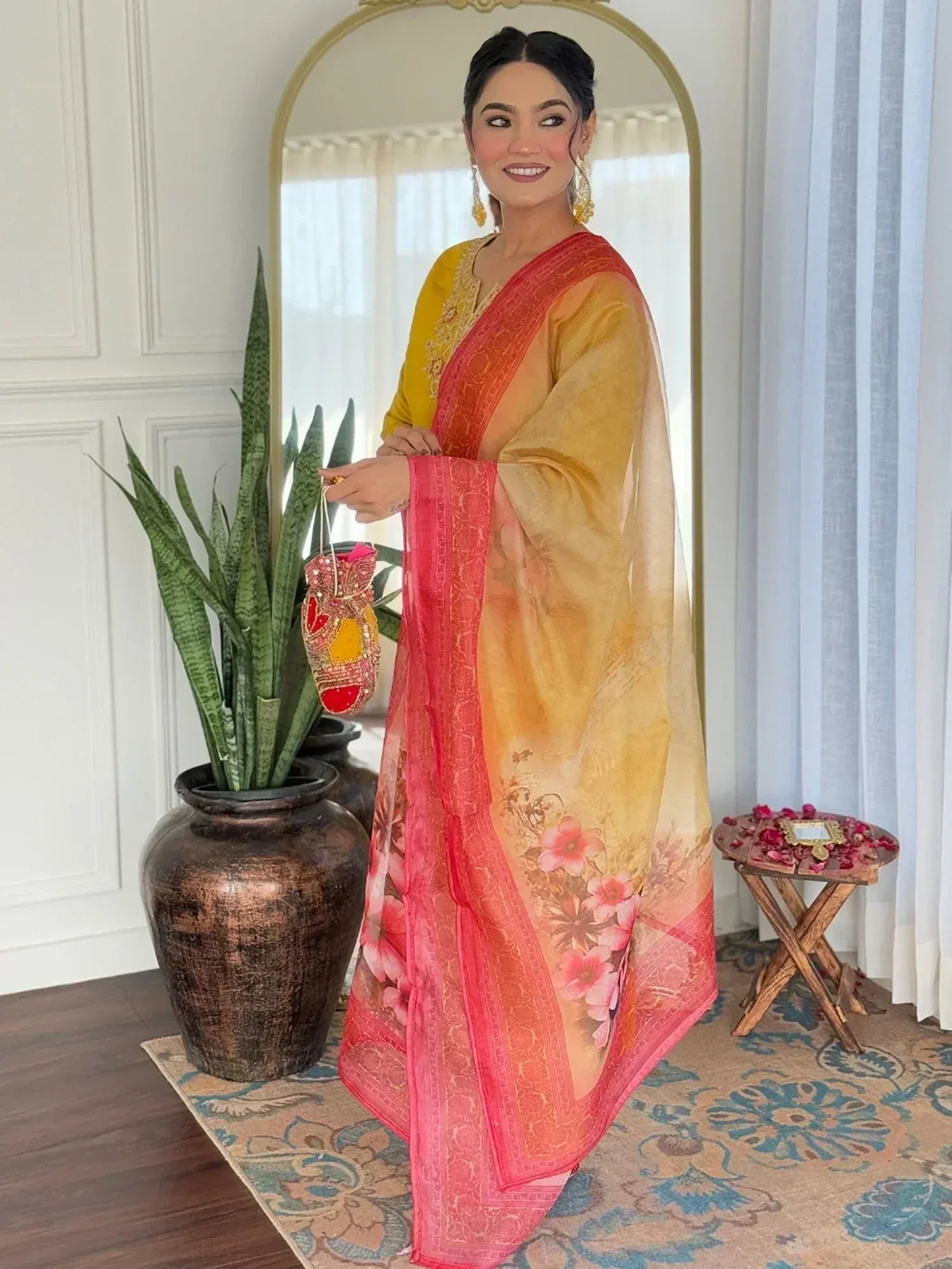 Woman in yellow and pink floral ethnic saree with embroidered blouse, holding embellished potli bag