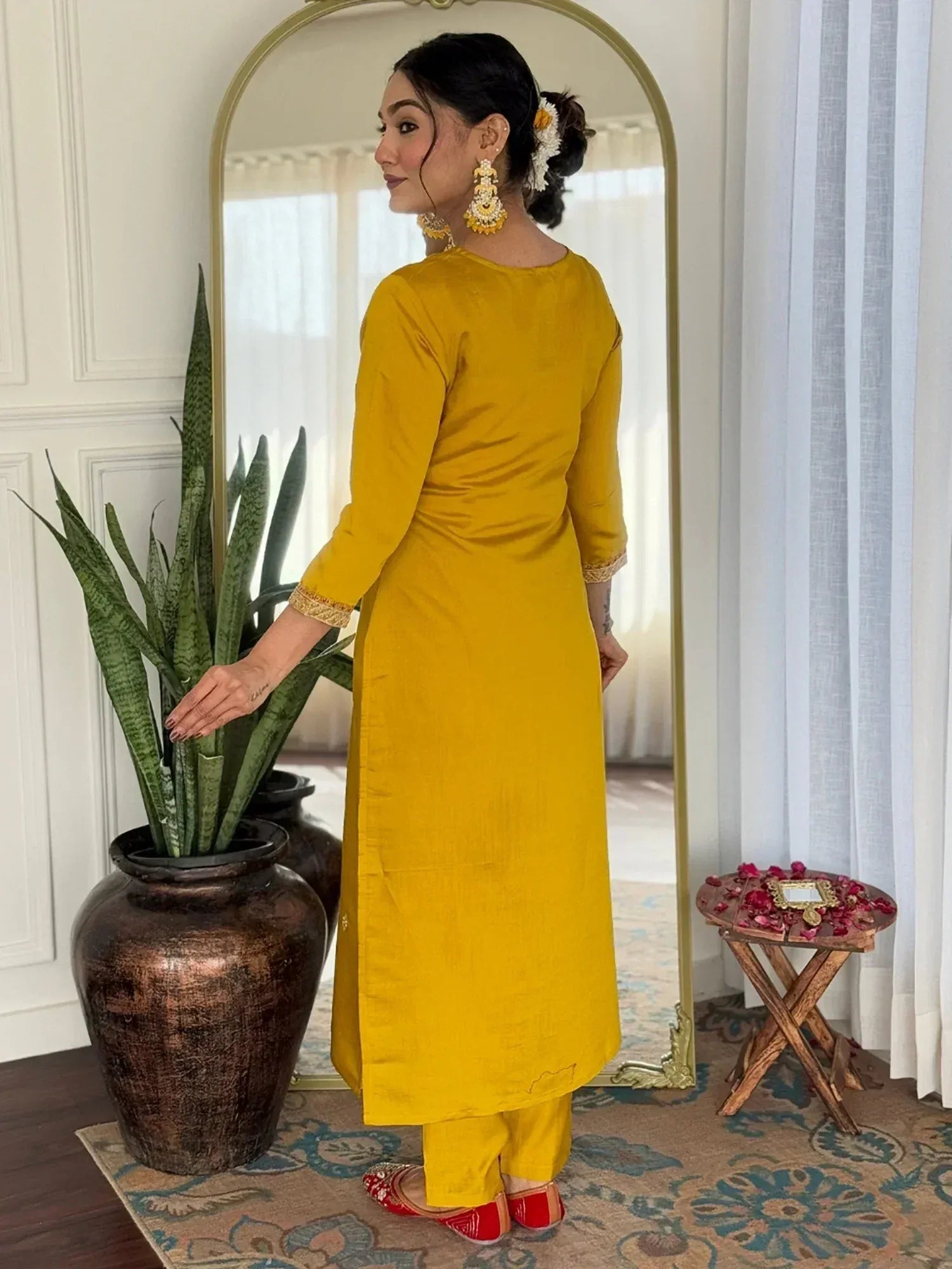 Woman in mustard yellow ethnic kurta with gold trim, matching pants, red flats, and floral hair accessory