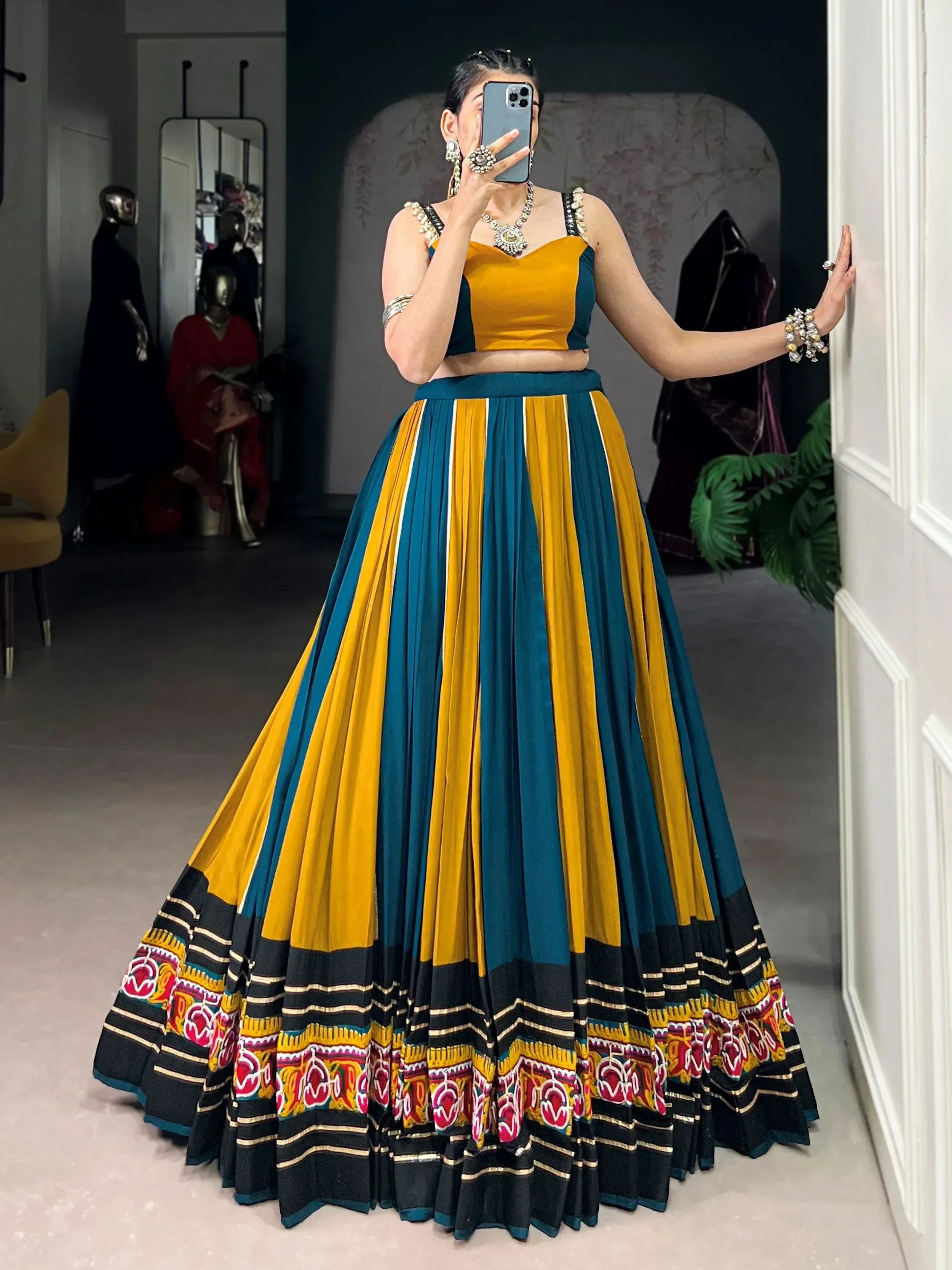 Woman in vibrant yellow and teal lehenga choli with embroidered border, perfect for Indian ethnic wear occasions.