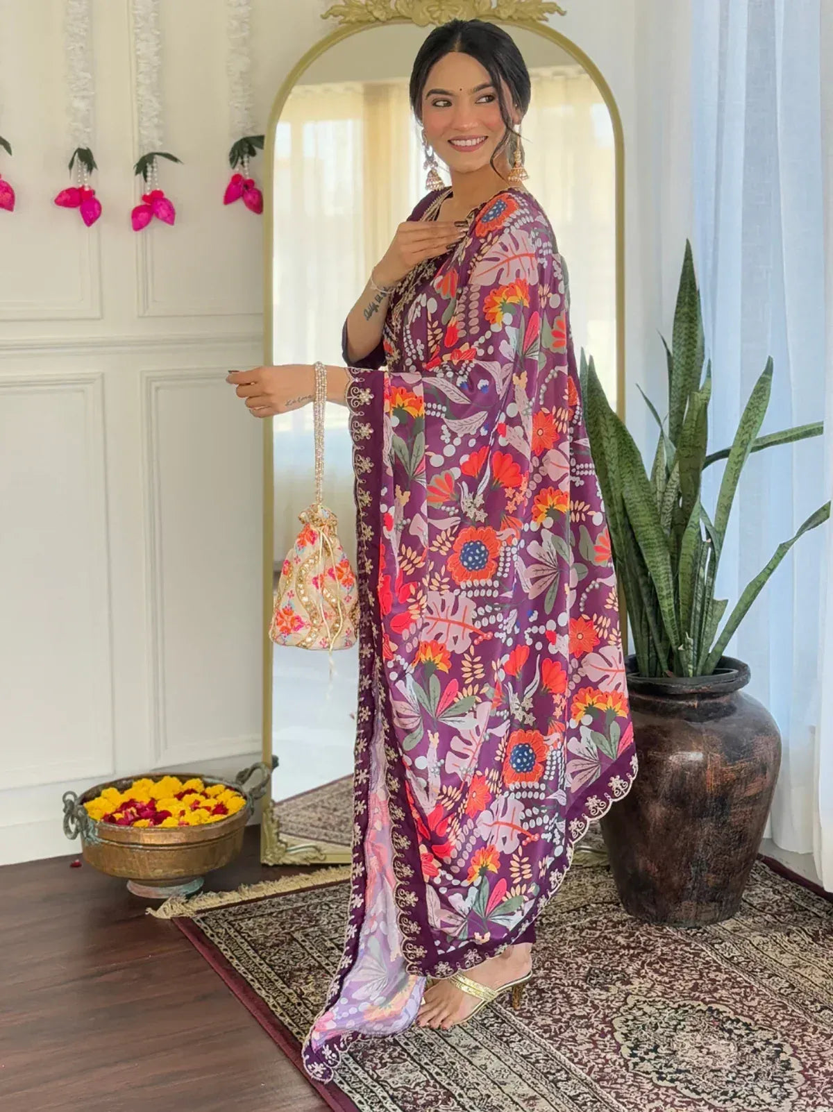 Woman in vibrant floral printed purple ethnic gown with matching potli bag, perfect for Indian occasions.