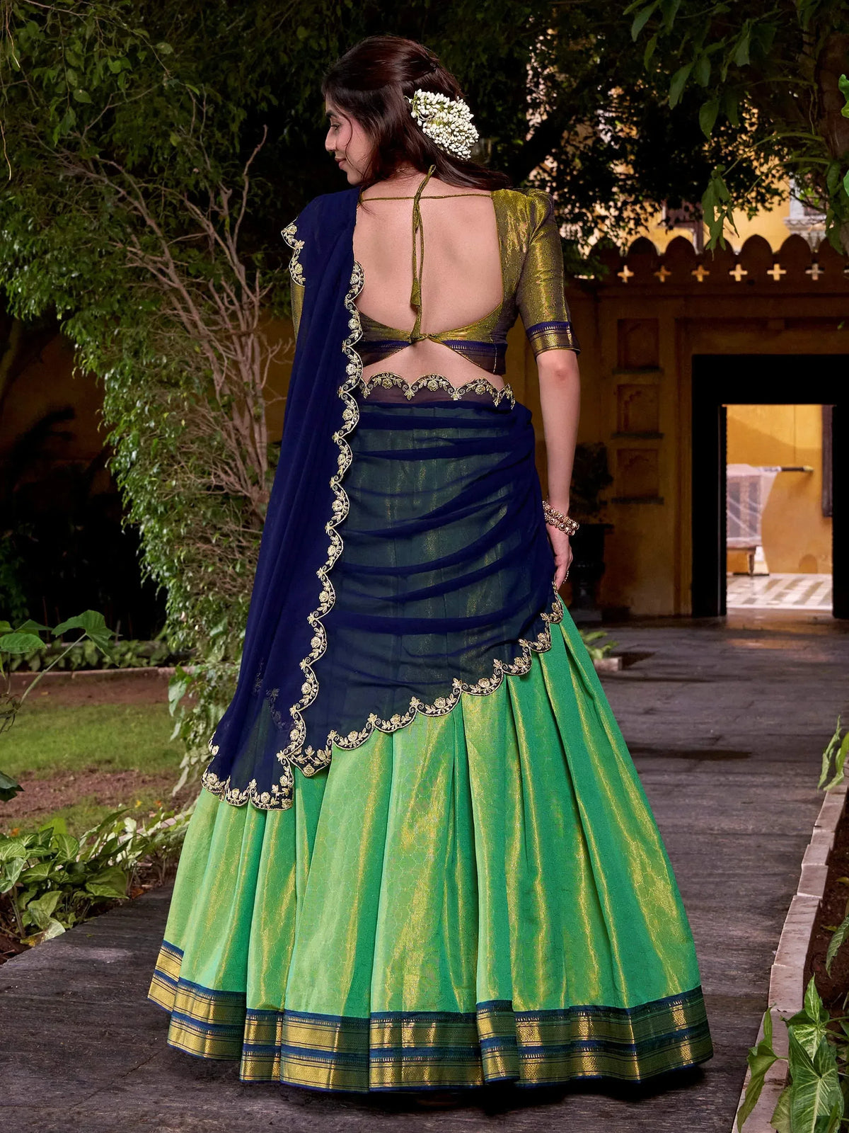Elegant green and navy blue lehenga choli with gold embroidery, backless blouse, and floral hair accessory