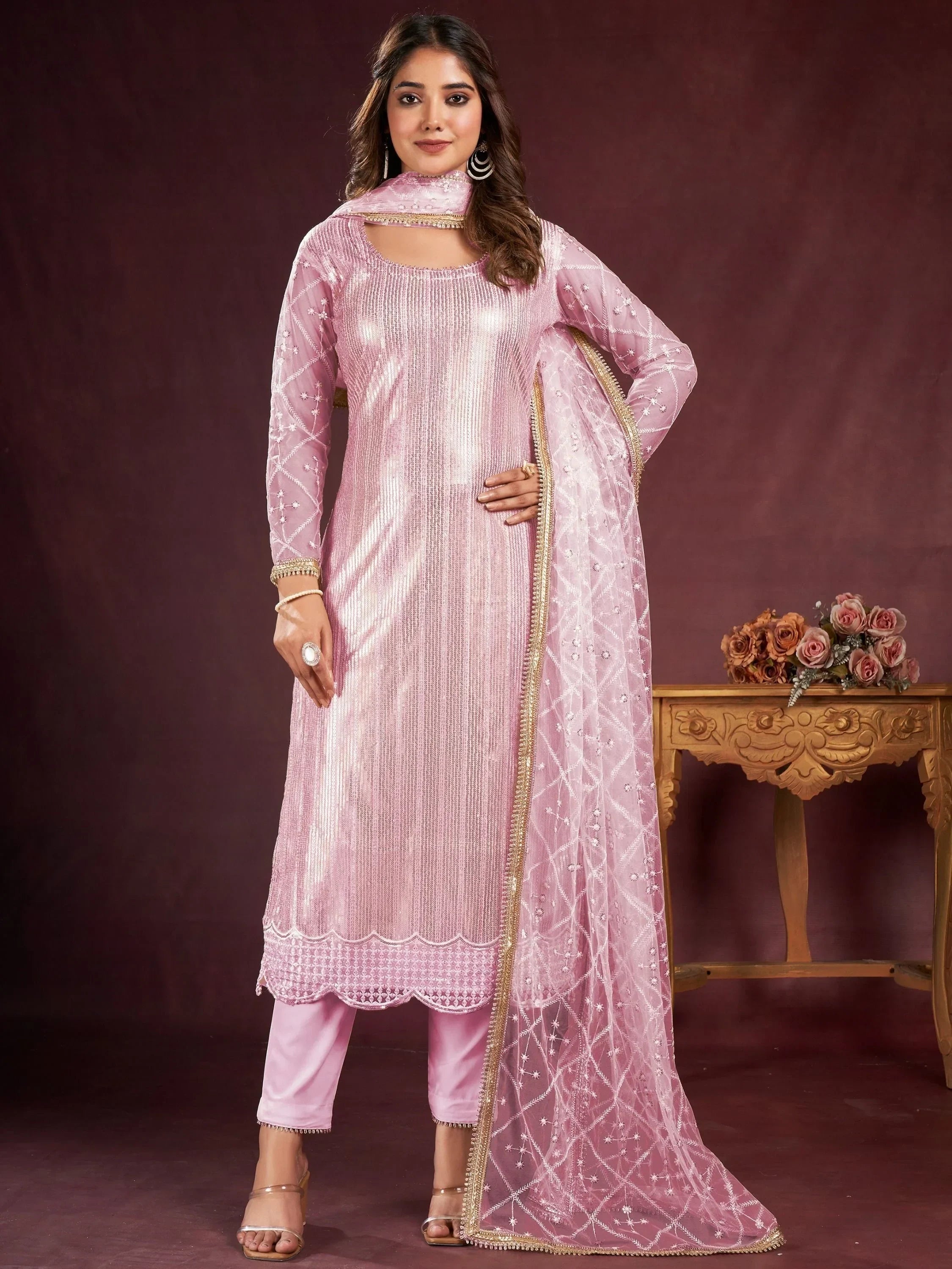 Woman in a pink embroidered salwar kameez with sheer dupatta, standing indoors