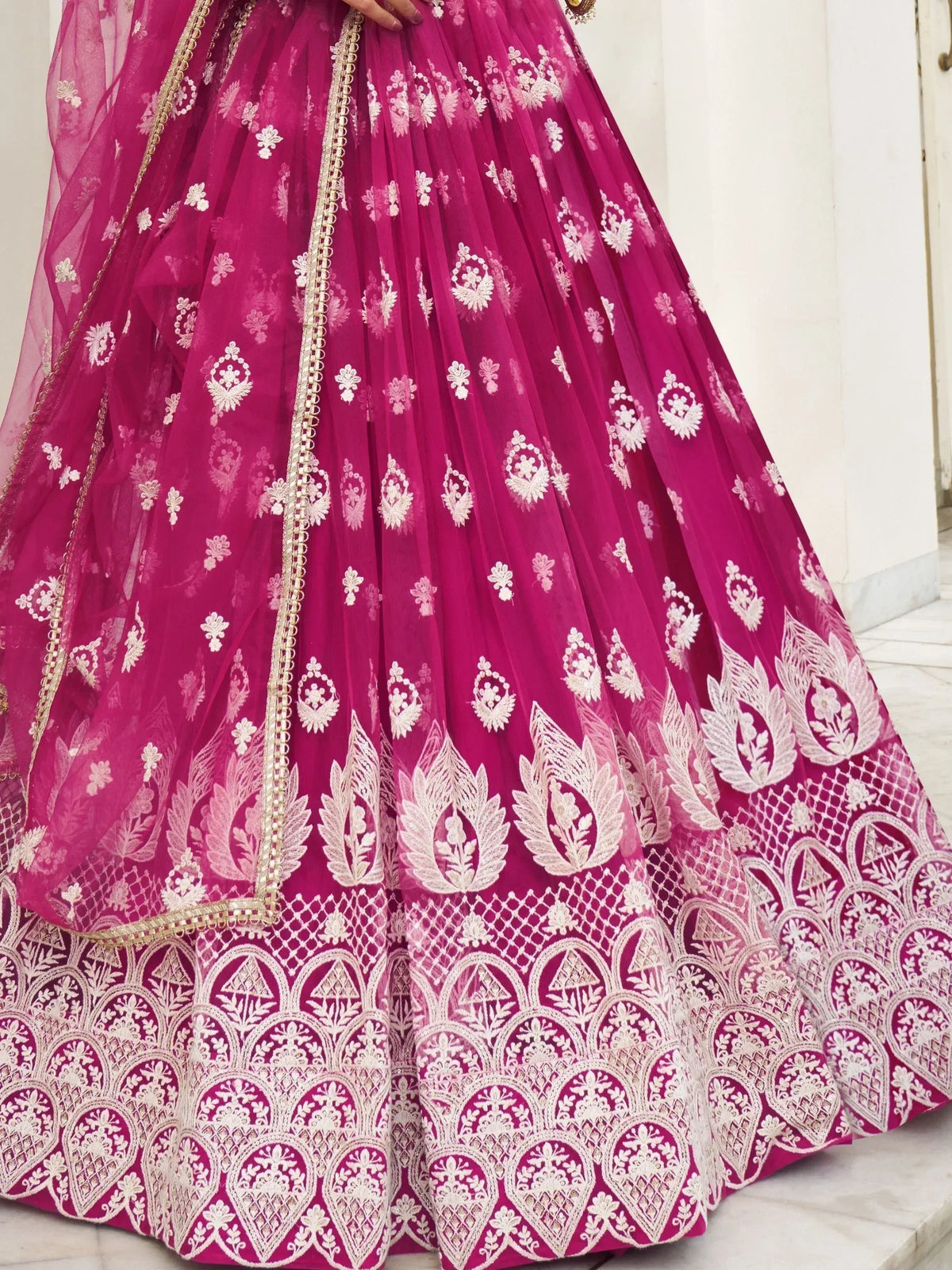 Fuchsia lehenga with intricate white embroidery and gold trim, perfect for Indian weddings and festive occasions.