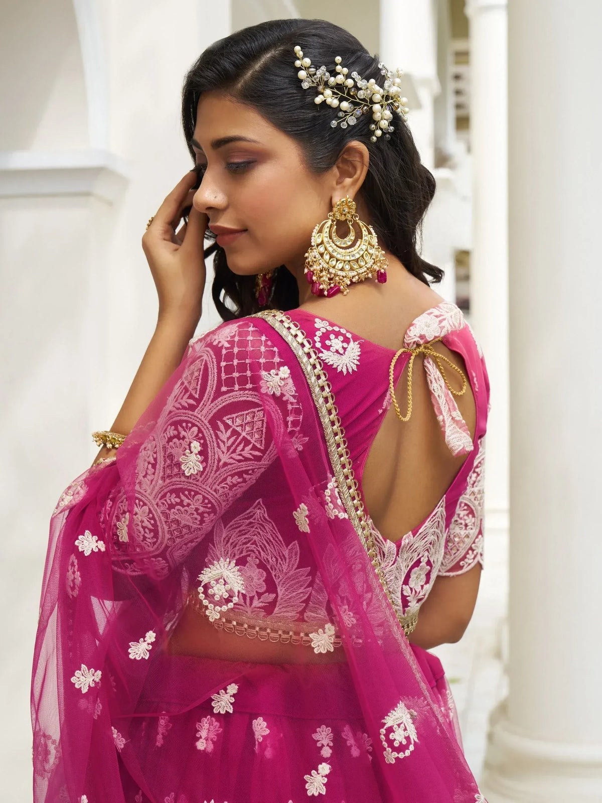 Pink embroidered lehenga choli with gold jewelry and floral hair accessory for Indian ethnic wear