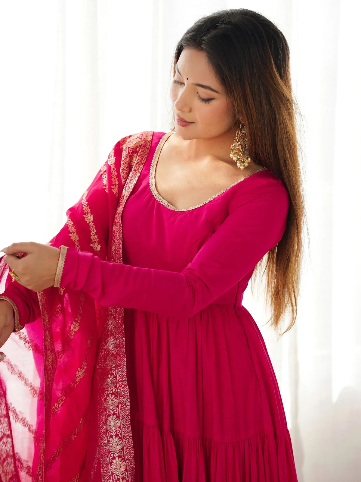 Woman in vibrant pink ethnic gown with gold embroidery, styled with traditional earrings for festive occasions