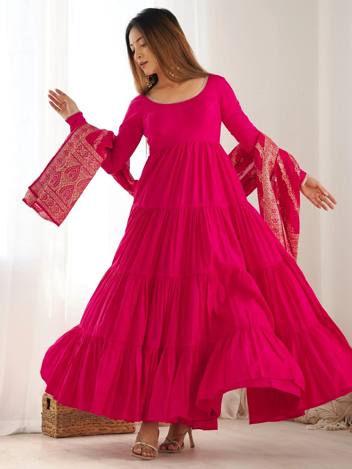 Vibrant pink tiered ethnic gown with gold-embroidered bell sleeves, perfect for festive occasions