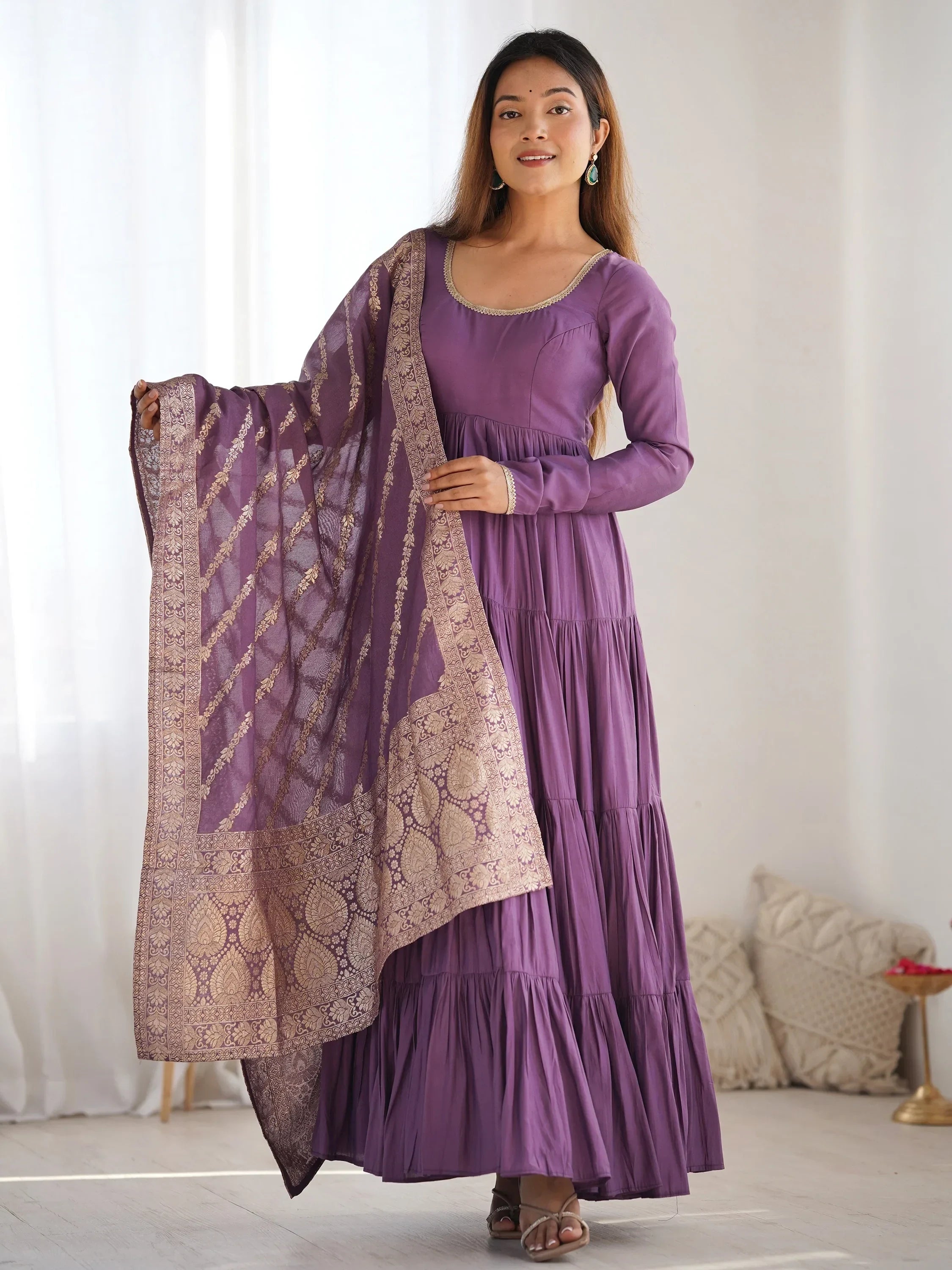 Woman in purple ethnic gown with gold embroidered dupatta, standing indoors