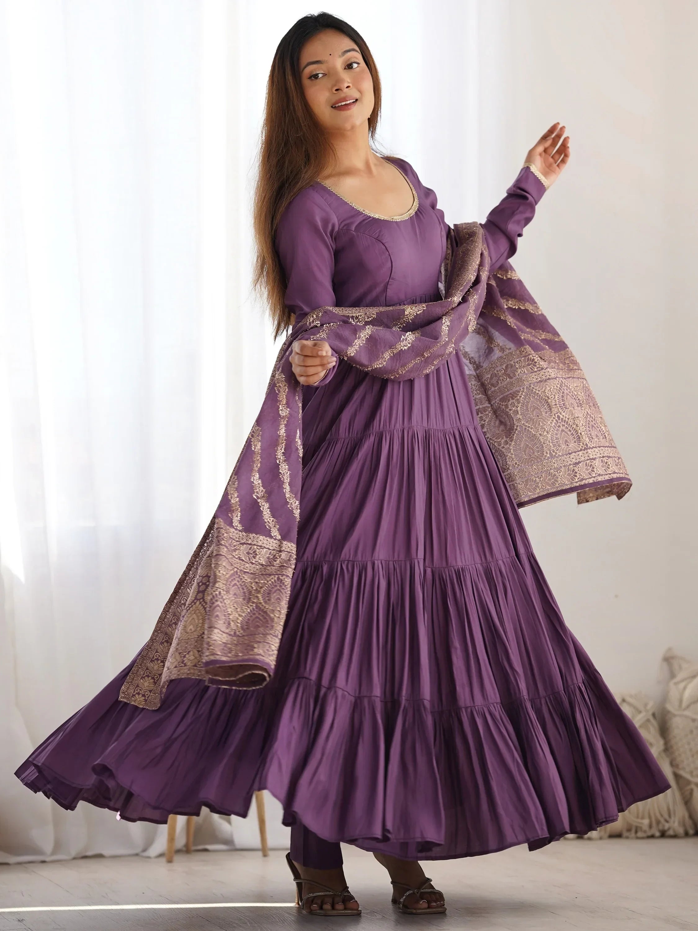 Woman in a flowy purple ethnic gown with long sleeves and gold embroidered dupatta
