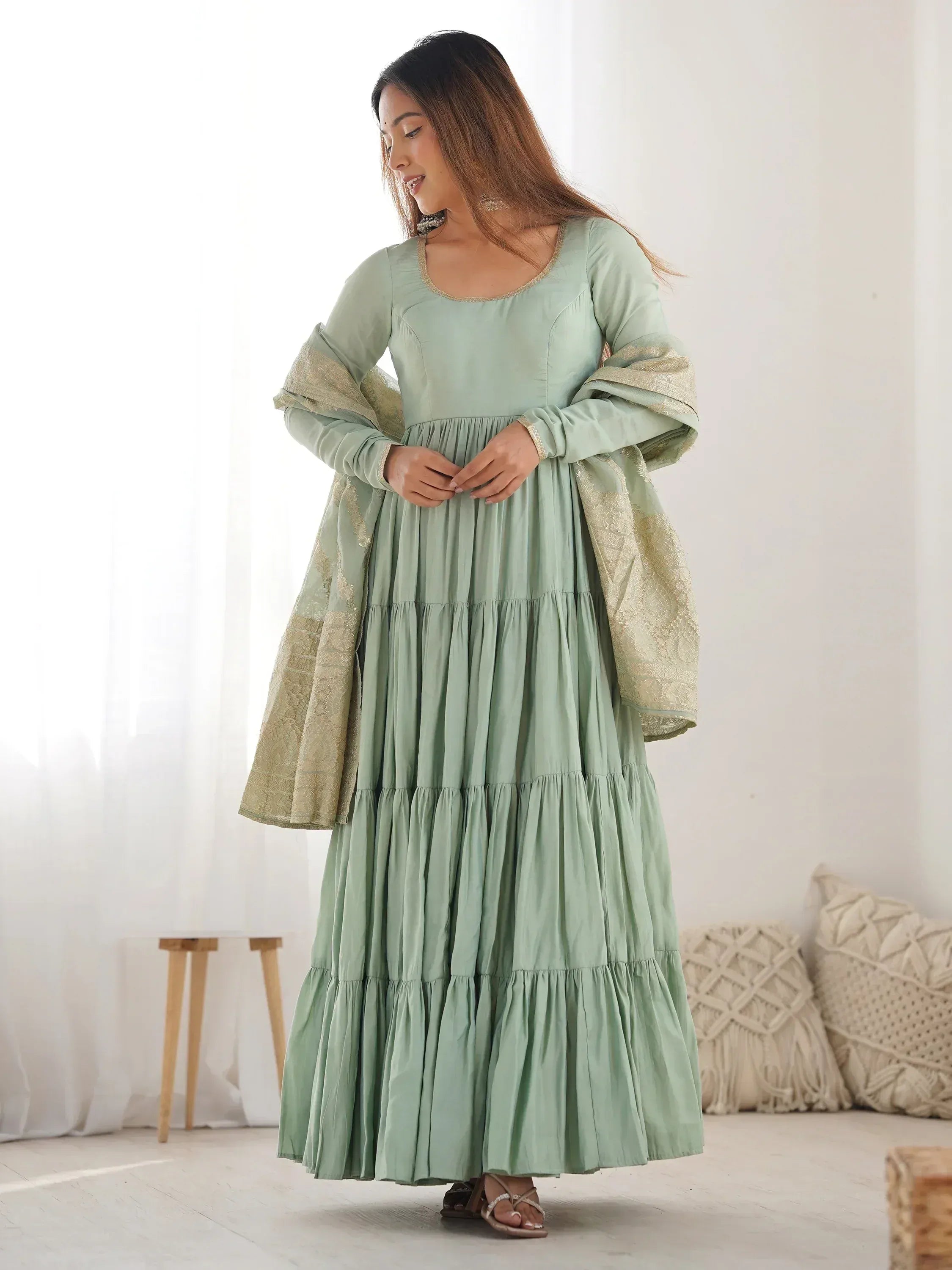 Woman wearing a sage green ethnic gown with dupatta, standing in a bright room