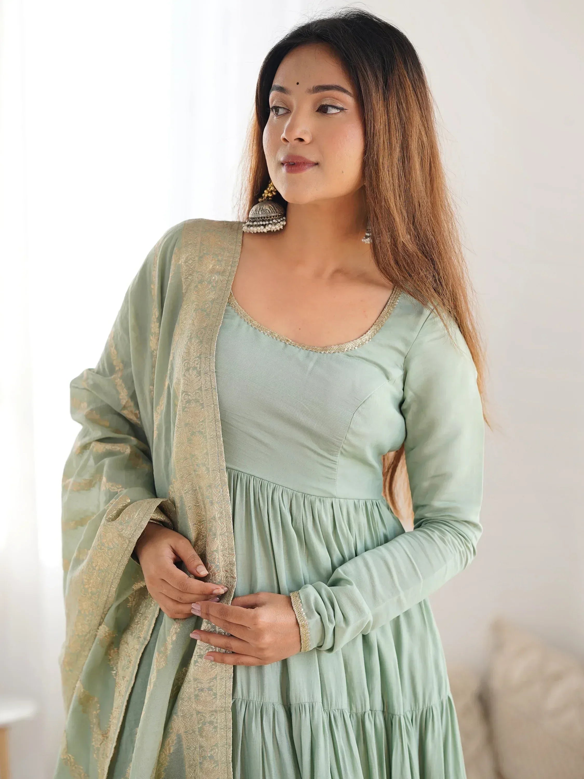 Woman wearing light green ethnic anarkali suit with embroidered dupatta and jhumka earrings