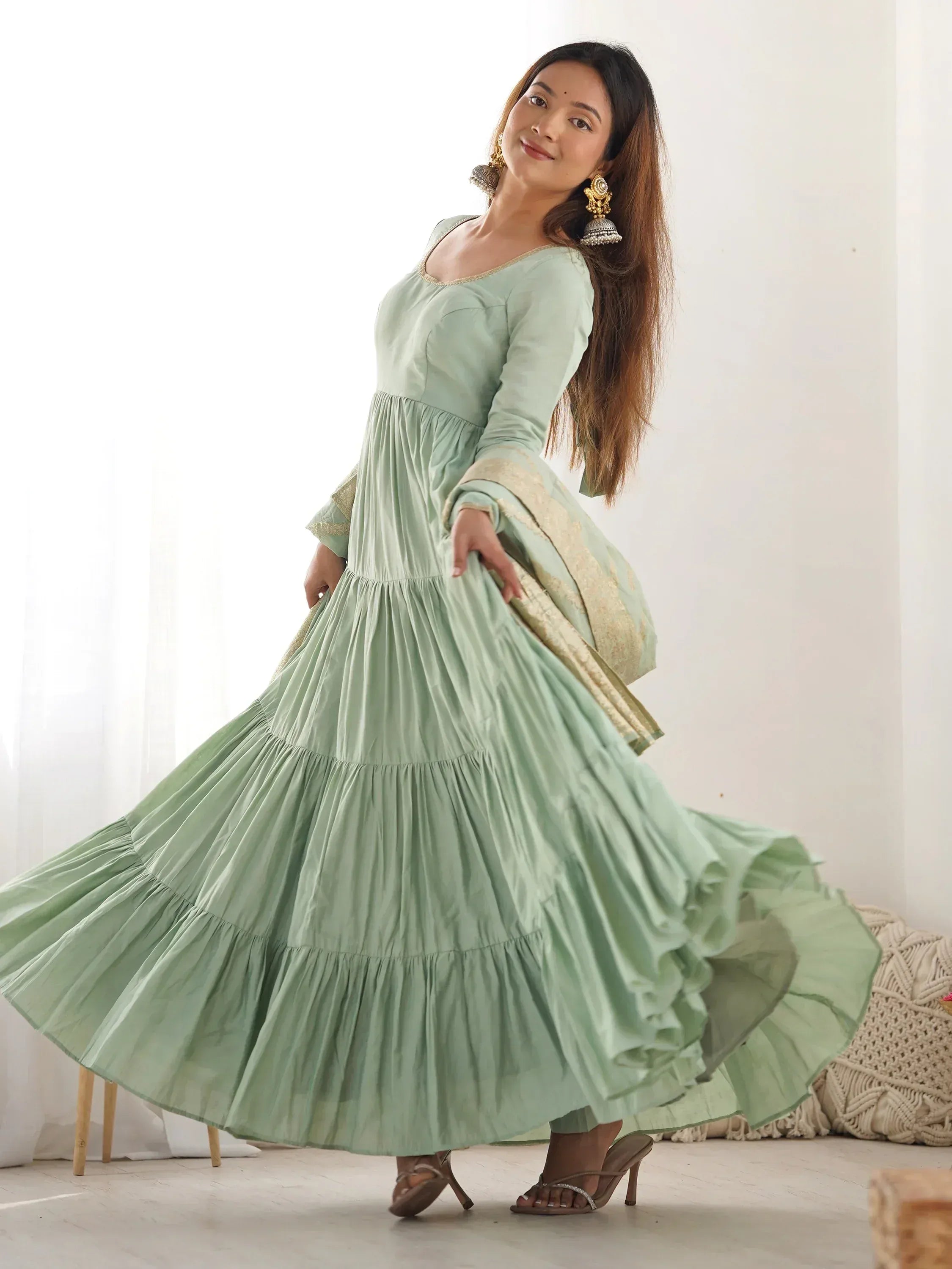 Woman in mint green flowy ethnic gown with gold border, traditional earrings, indoor setting