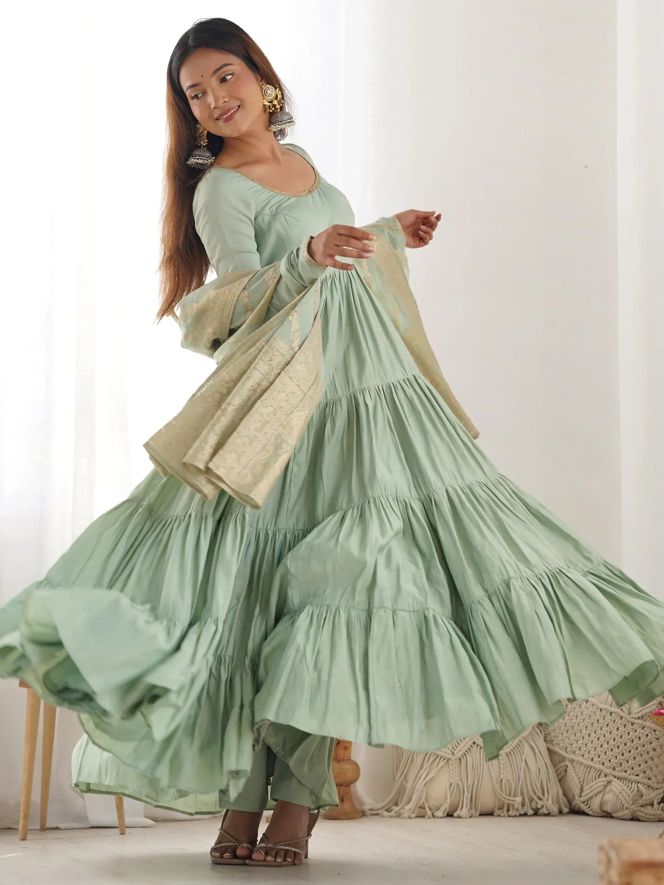 Woman twirling in a light green flared ethnic gown with gold dupatta and statement earrings