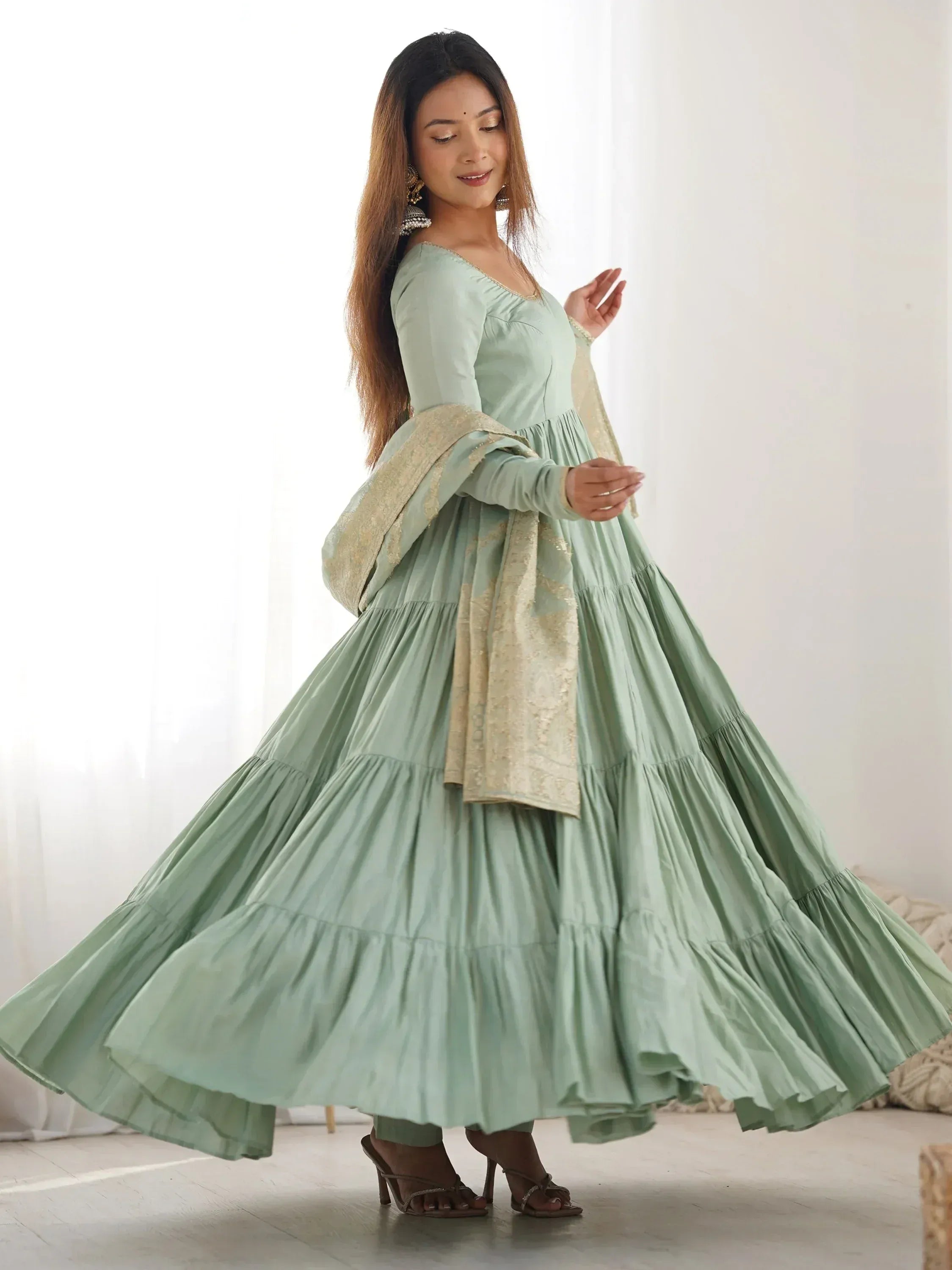 Woman twirling in a mint green ethnic gown with long sleeves and embroidered dupatta