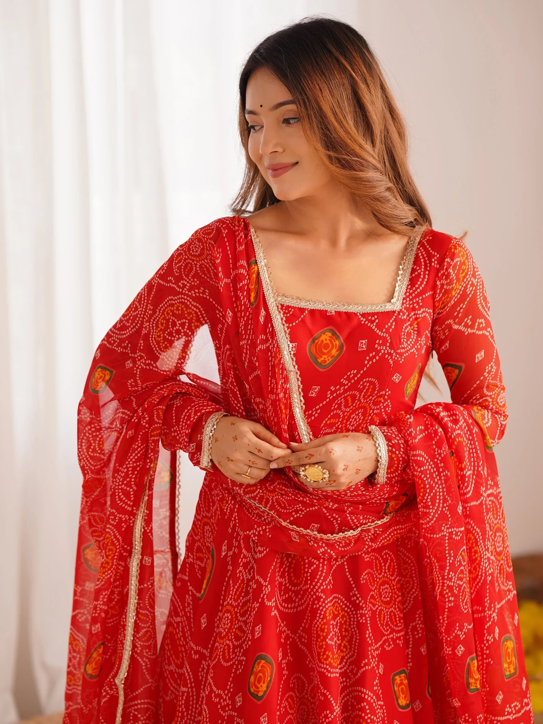 Woman wearing red bandhani ethnic gown with gold trim and traditional jewelry