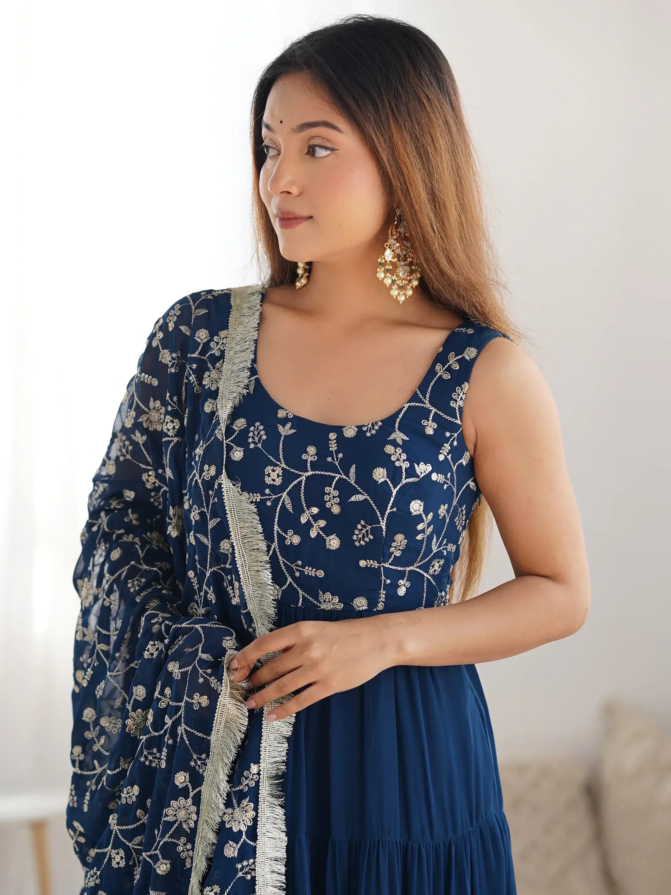 Woman in navy blue embroidered ethnic gown with matching dupatta and gold earrings