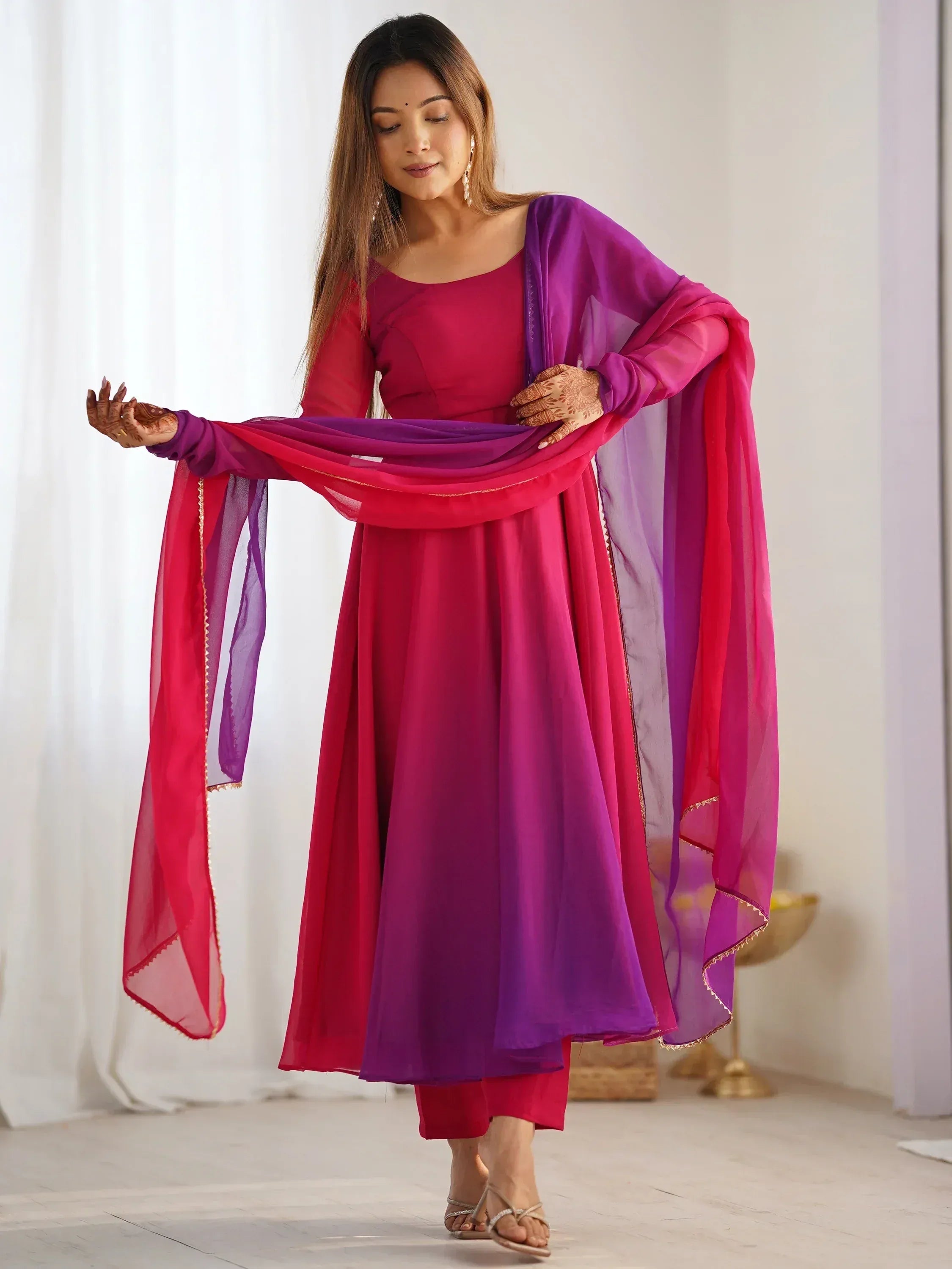 Woman in vibrant pink and purple Indian ethnic anarkali suit with sheer dupatta, perfect for festive occasions