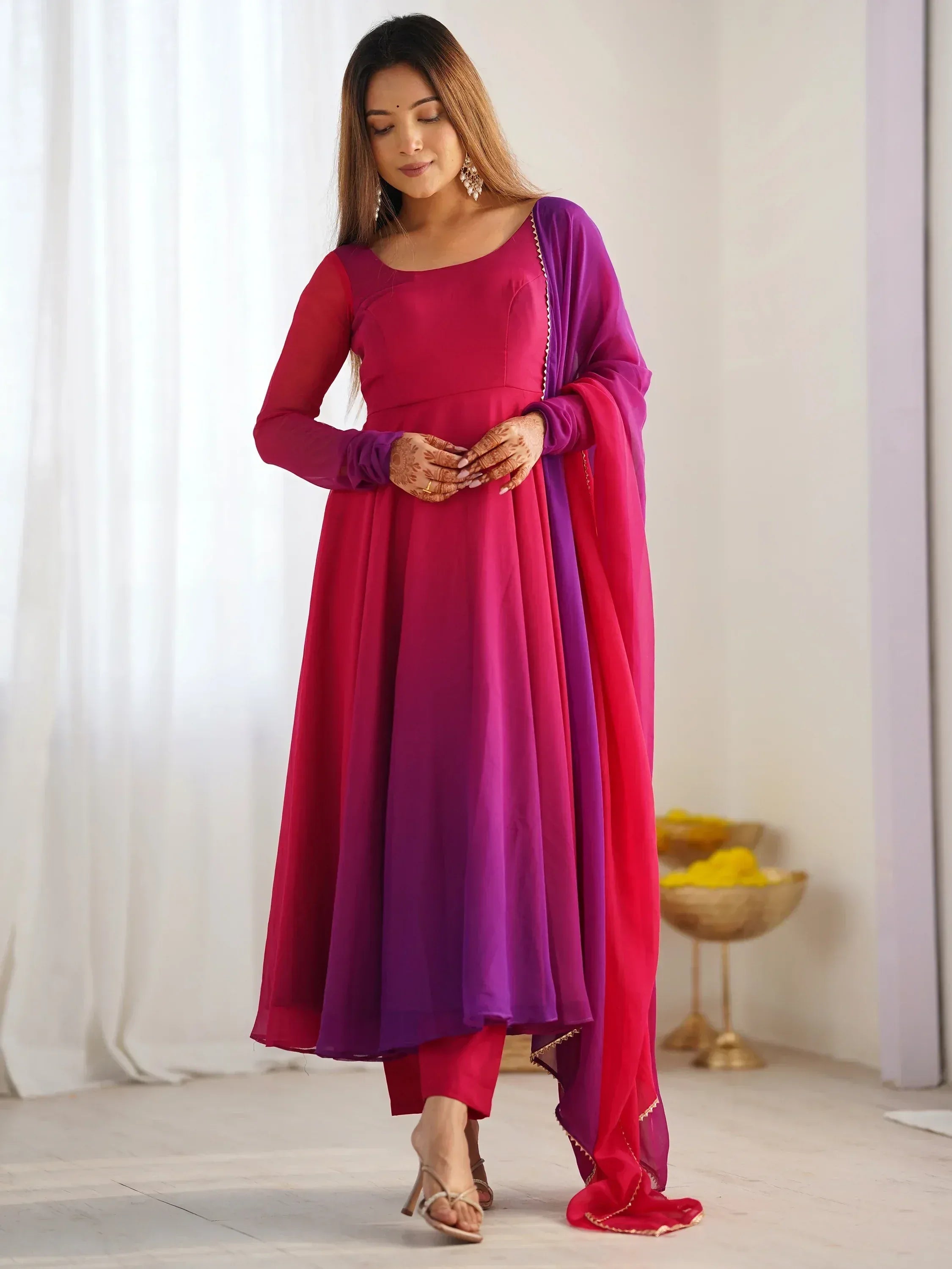 Woman in vibrant pink and purple Indian ethnic anarkali suit with matching dupatta, perfect for festive occasions.