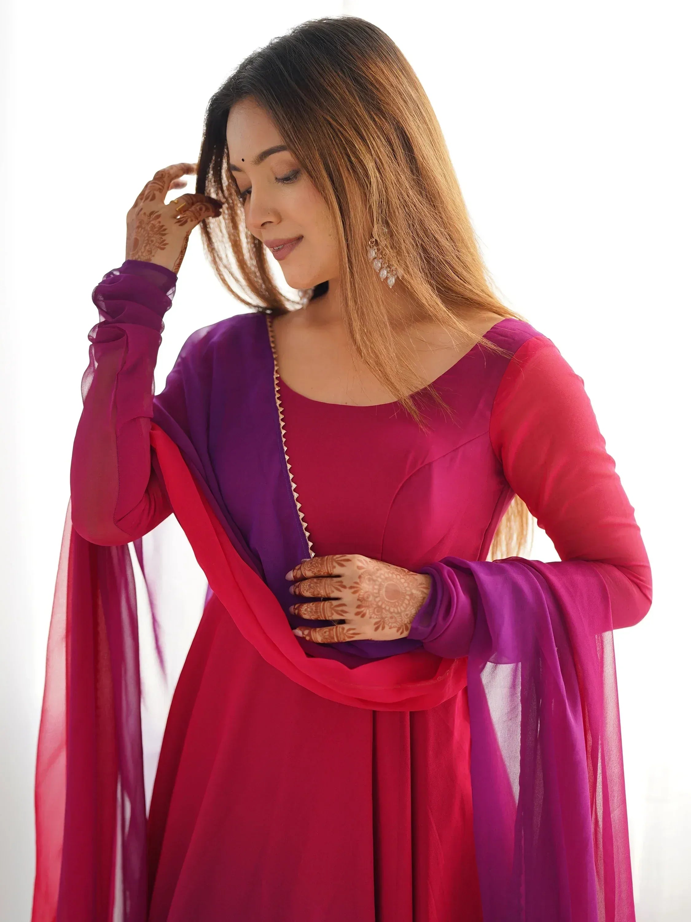 Woman in vibrant pink and purple ethnic gown with sheer sleeves and henna designs