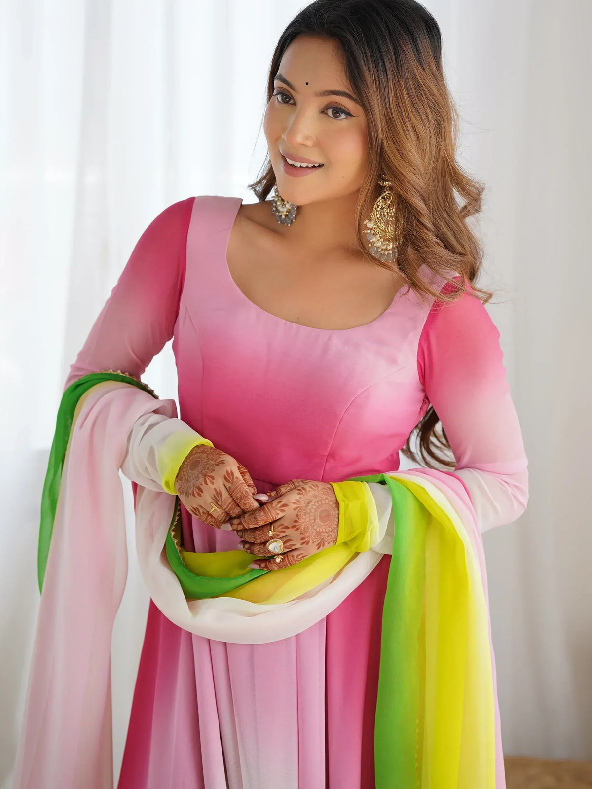 Woman in pink Indian ethnic gown with colorful dupatta, henna hands, and gold jewelry