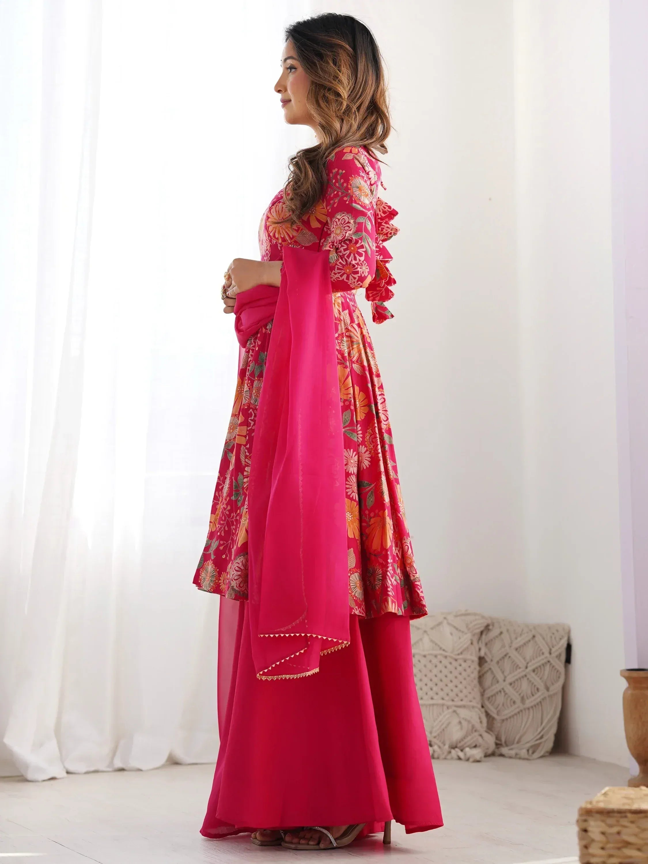 Woman in vibrant pink floral anarkali suit with ruffled sleeves and matching dupatta, ideal for Indian ethnic occasions.